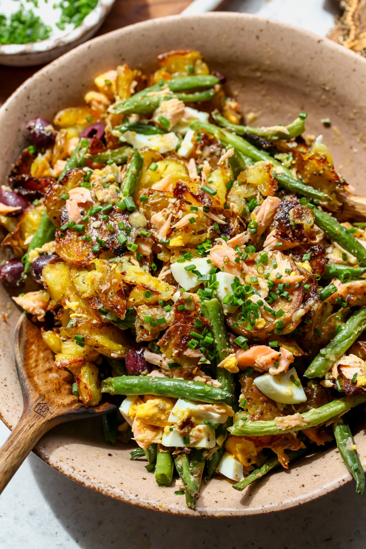 Salmon Niçoise Smashed Potato Salad being tossed in a light pink salad bowl.