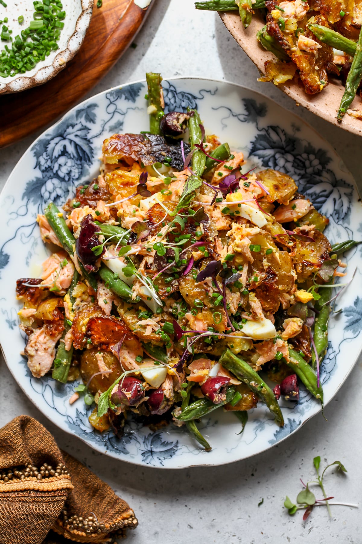 Salmon niçoise smashed potato salad styled on a white and blue floral plate.