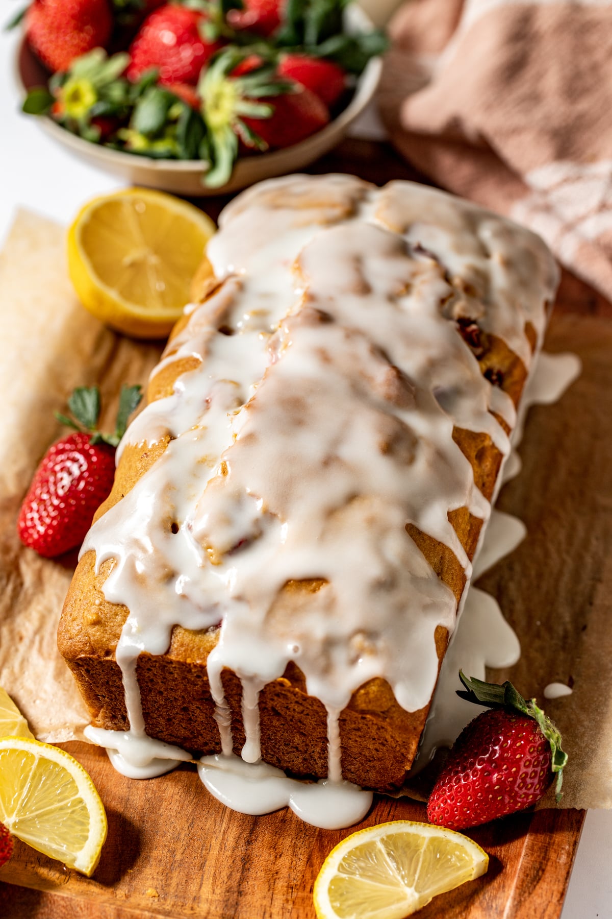 A loaf of strawberry lemon glaze topped with lemony glaze arranged on a wooden cutting board.
