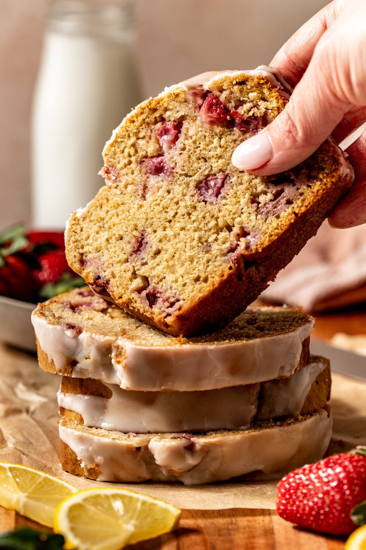 A stack of strawberry lemon bread slices with one being lifted off the top by hand.