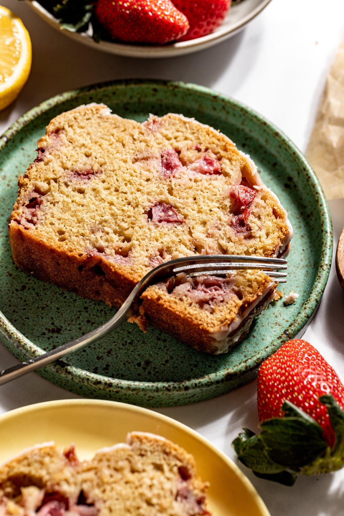A slice of strawberry lemon bread on a green plate with a fork resting on the right side.