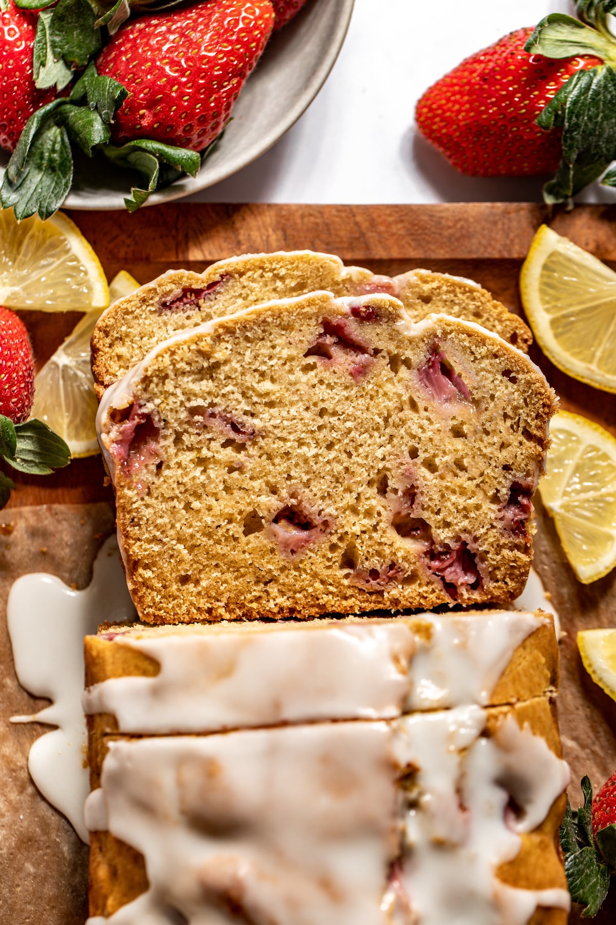 Sliced strawberry lemon bread styled on a wooden cutting board with lemon slices arranged on the sides.
