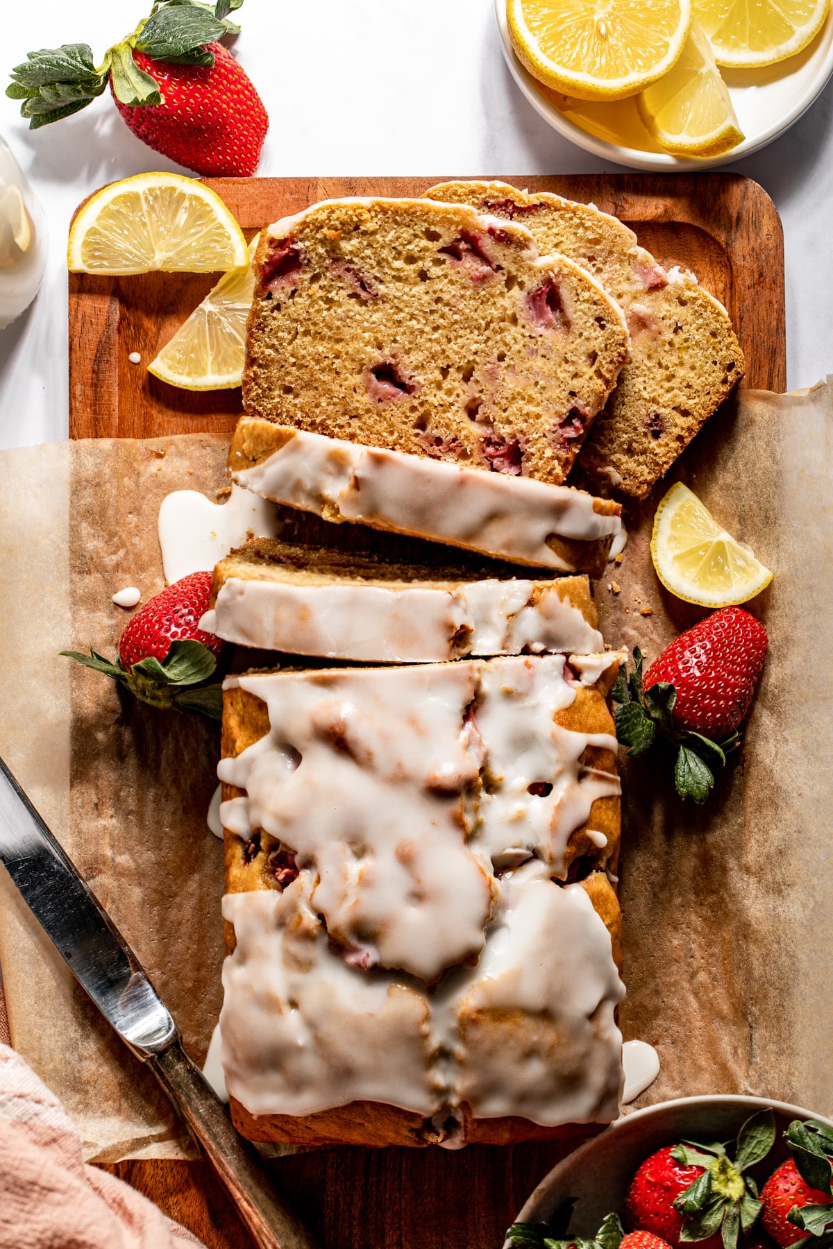 Strawberry Lemon Bread sliced on a cutting board surrounded by strawberries and lemon slices.