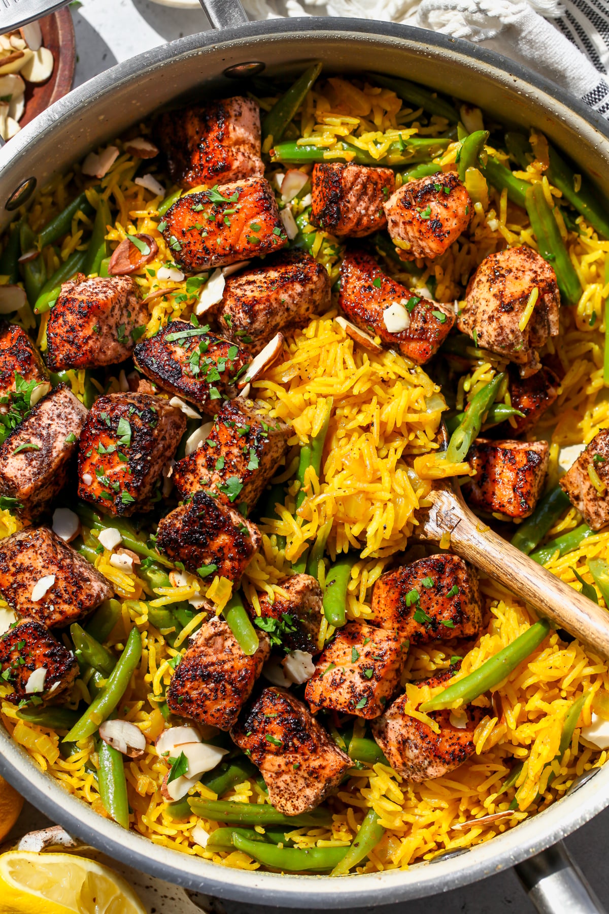 A wooden serving spoon stirring into a pan of golden rice and salmon.