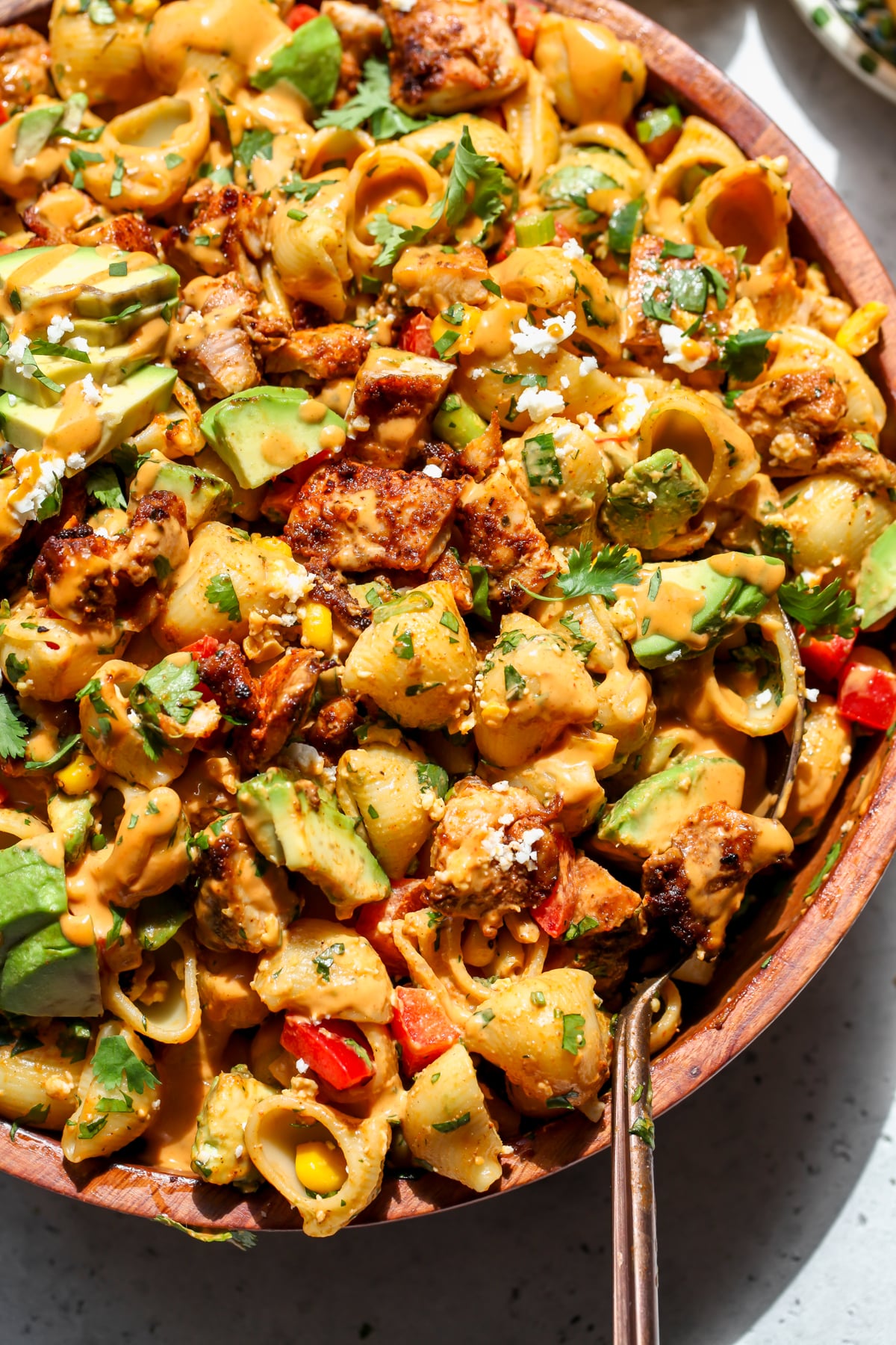 A gold serving spoon resting on the right side of a bowl of chipotle tahini pasta salad.