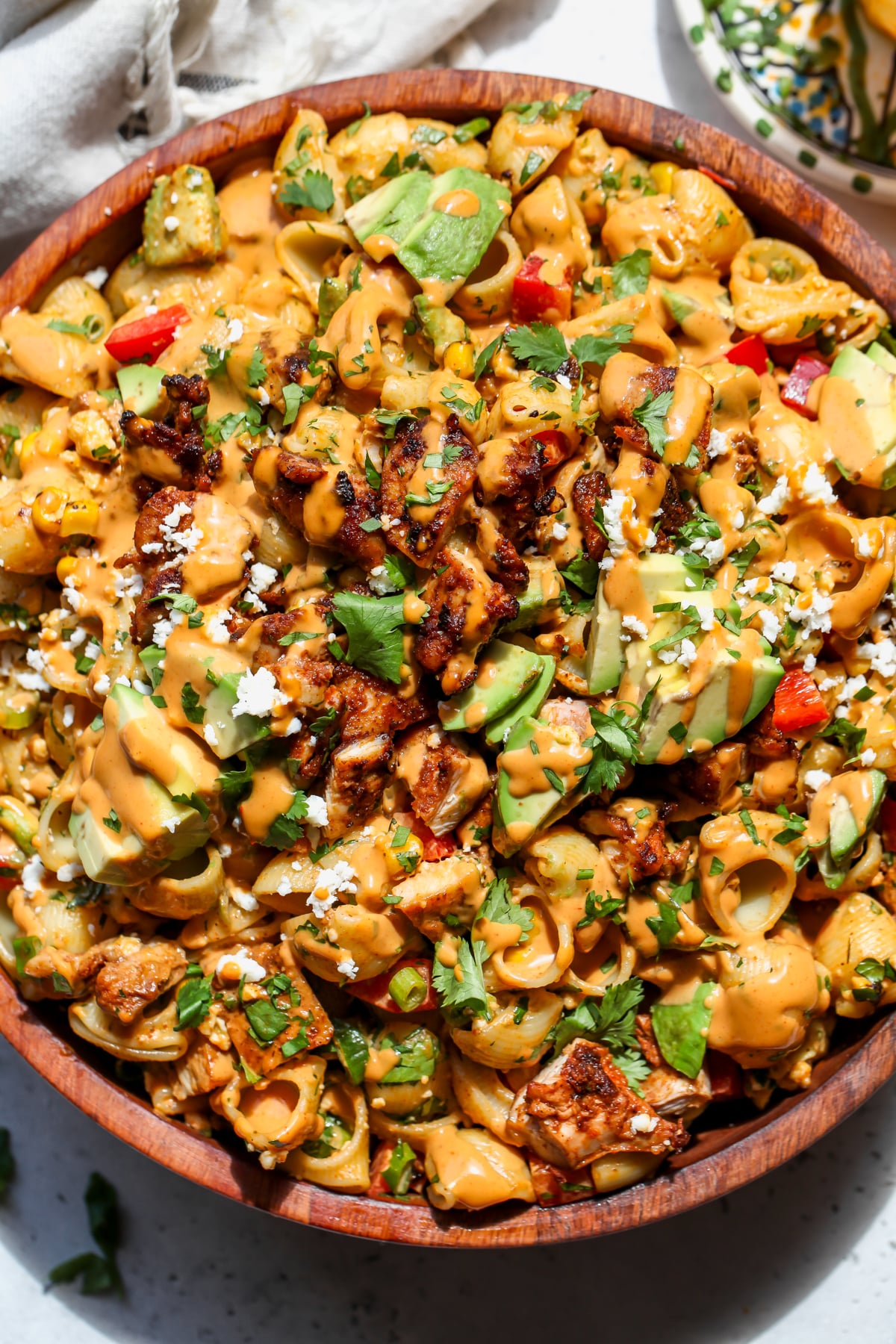 Chipotle pasta salad styled in a large wooden bowl topped with avocado slices, cotija cheese, and cilantro.
