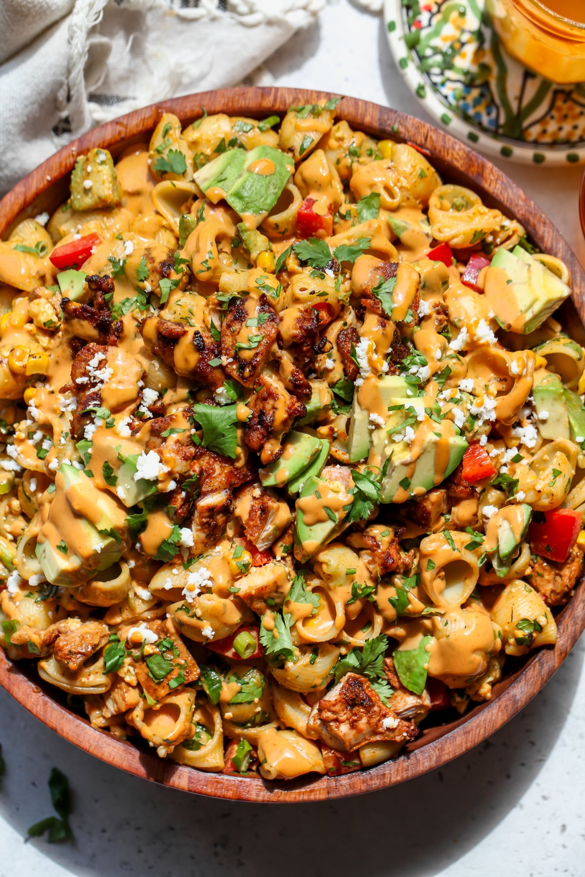 Chipotle-Tahini Pasta Salad styled in a wooden serving bowl topped with avocado slices.