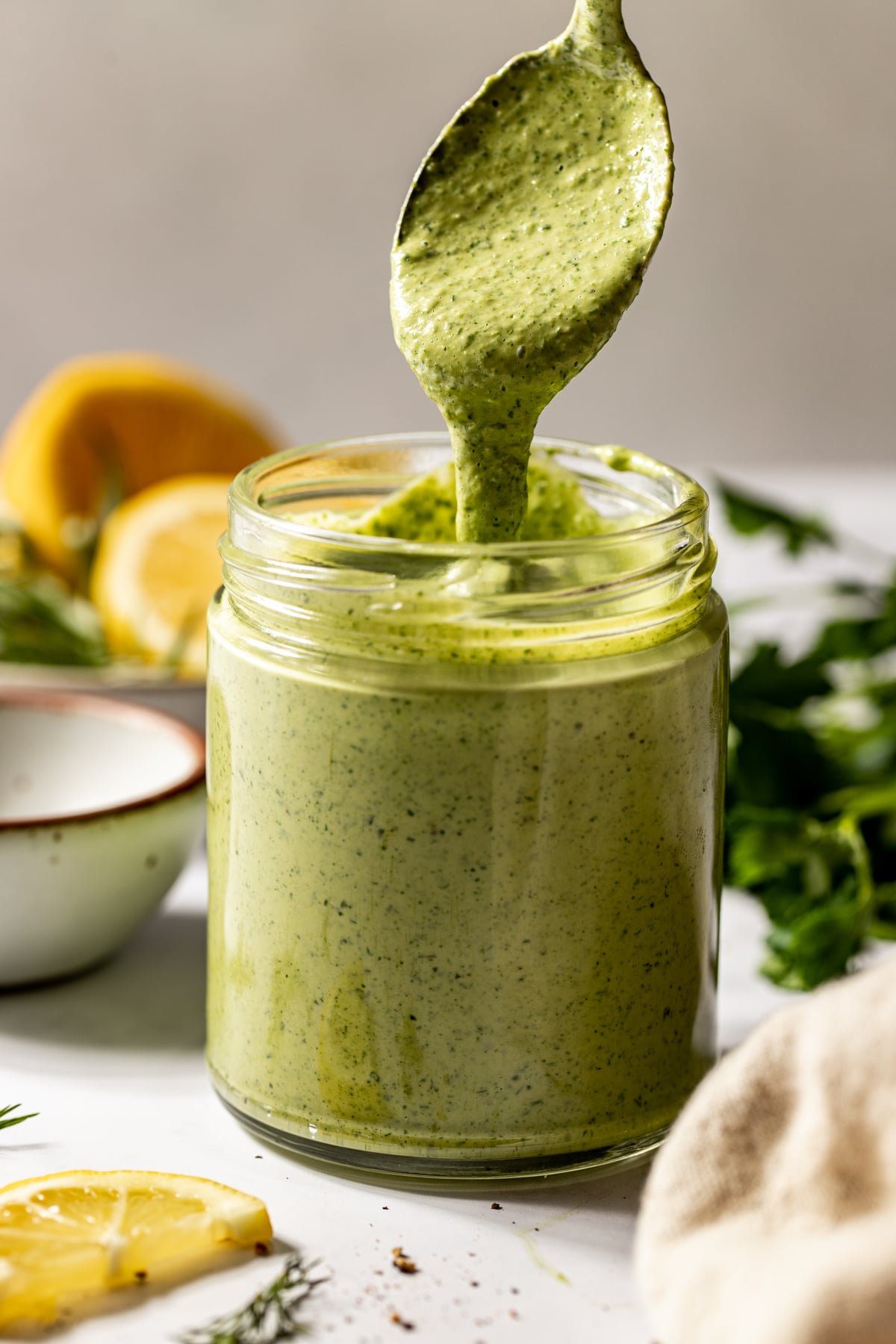 A spoon drizzling green goddess tahini dressing into a glass storage jar.