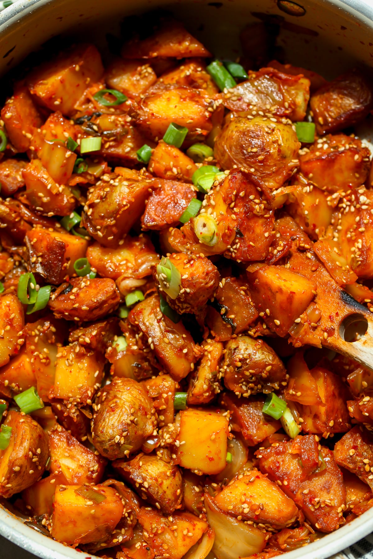 Kimchi potatoes topped with green onion in a sauté pan.