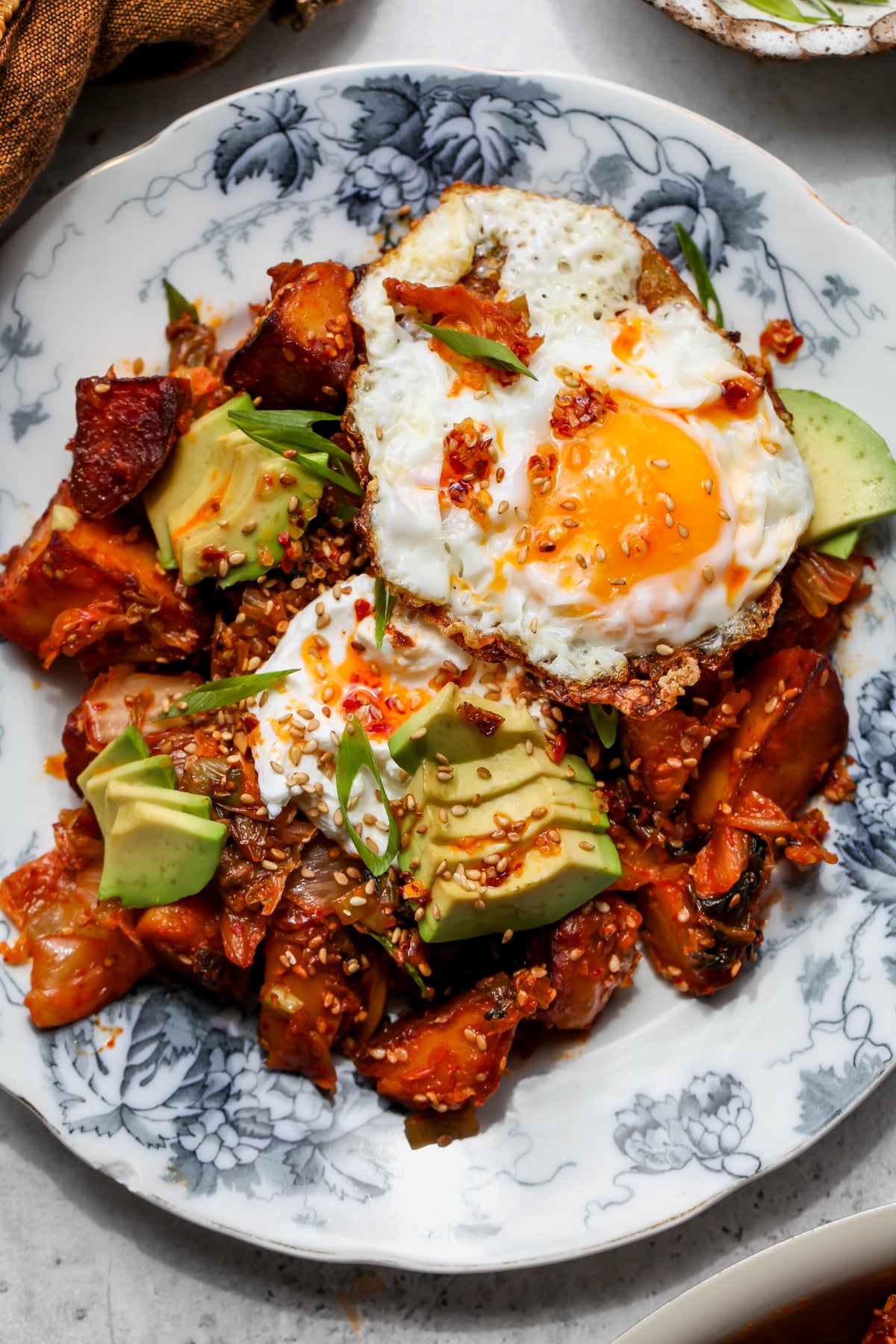 A plate of kimchi potatoes topped with garlicky yogurt, sliced avocado, and a crispy fried egg.