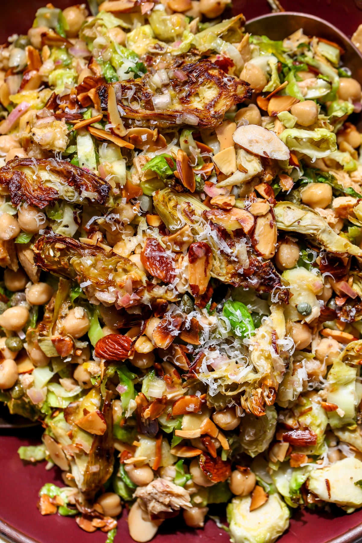 Roasted artichoke salad with Brussels sprouts, almonds, tuna, and chickpeas tossed in a maroon serving bowl.