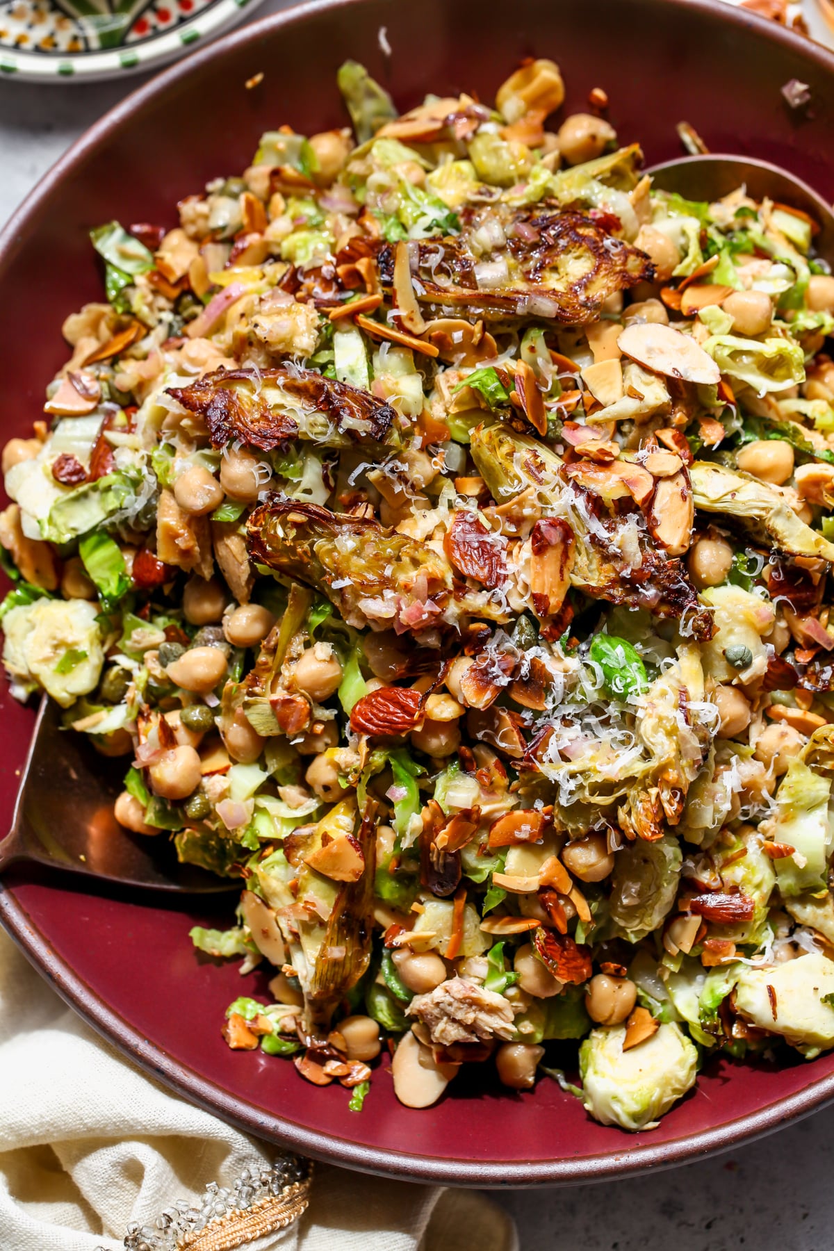 Roasted artichoke salad styled in a maroon bowl with Brussels sprouts, chickpeas, and tuna.