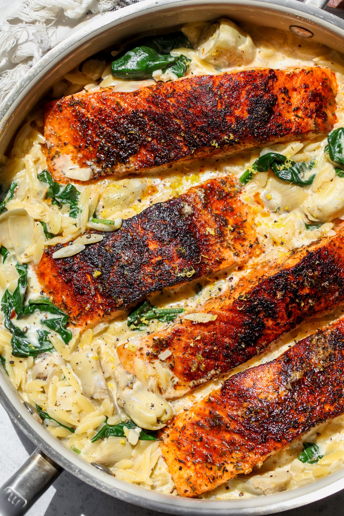 Spinach artichoke salmon and orzo arranged in a sauté pan.