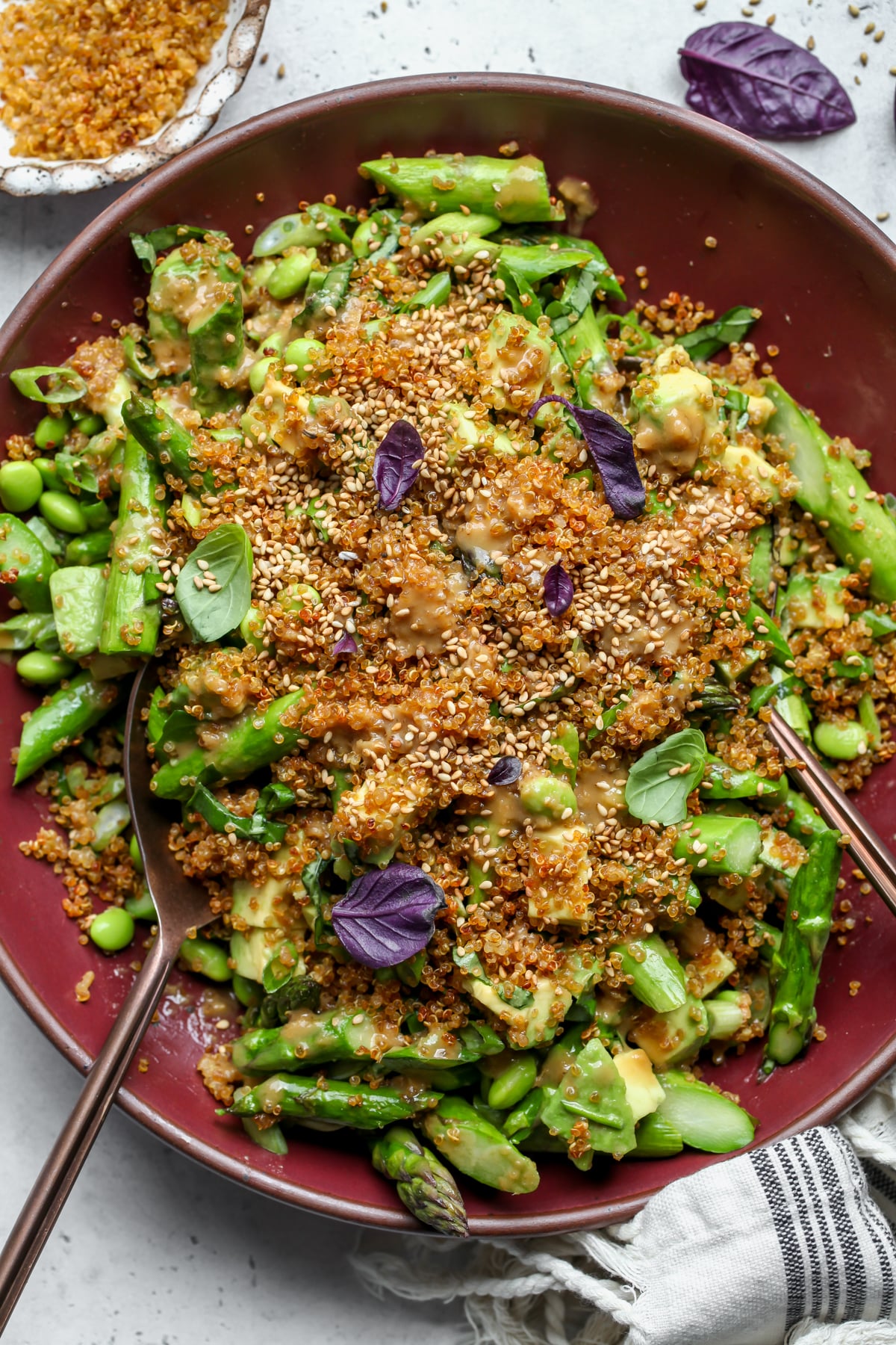 Crispy quinoa salad styled in a maroon serving bowl with gold utensils resting on each side of the bowl.