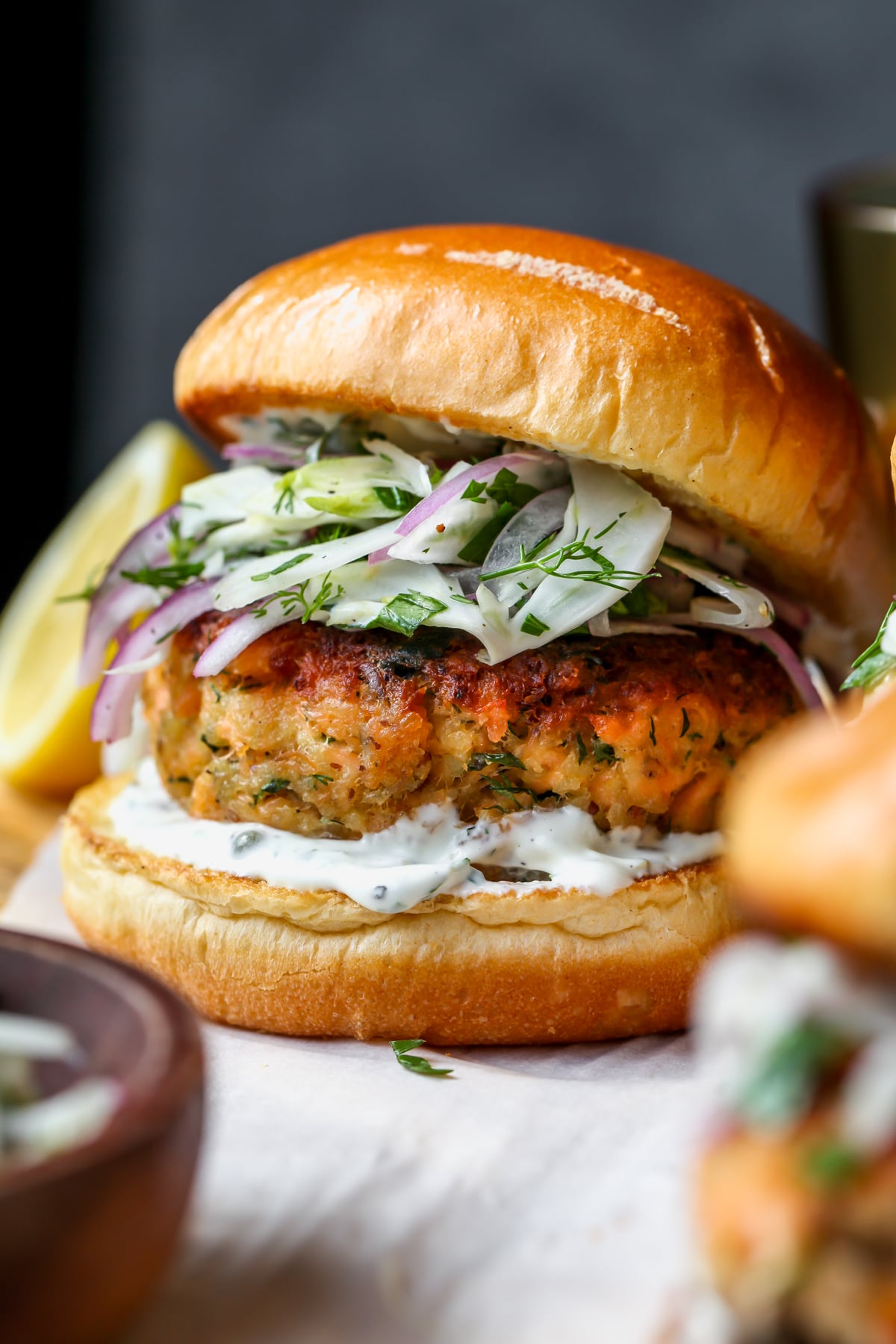 Salmon burger topped with fennel slaw styled on a wooden cutting board.