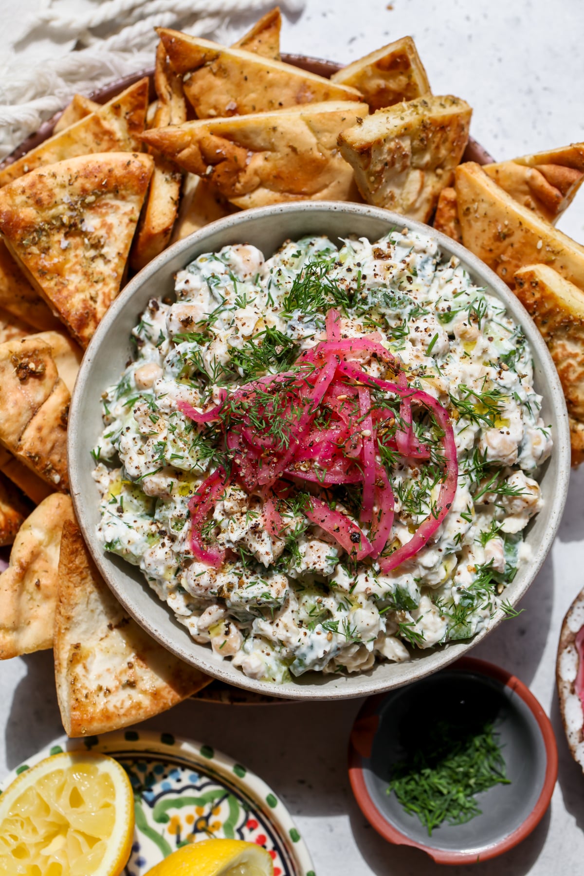 Tzatziki Chickpea Tuna Salad topped with pickled red onions in a white bowl surrounded by za'atar pita chips.