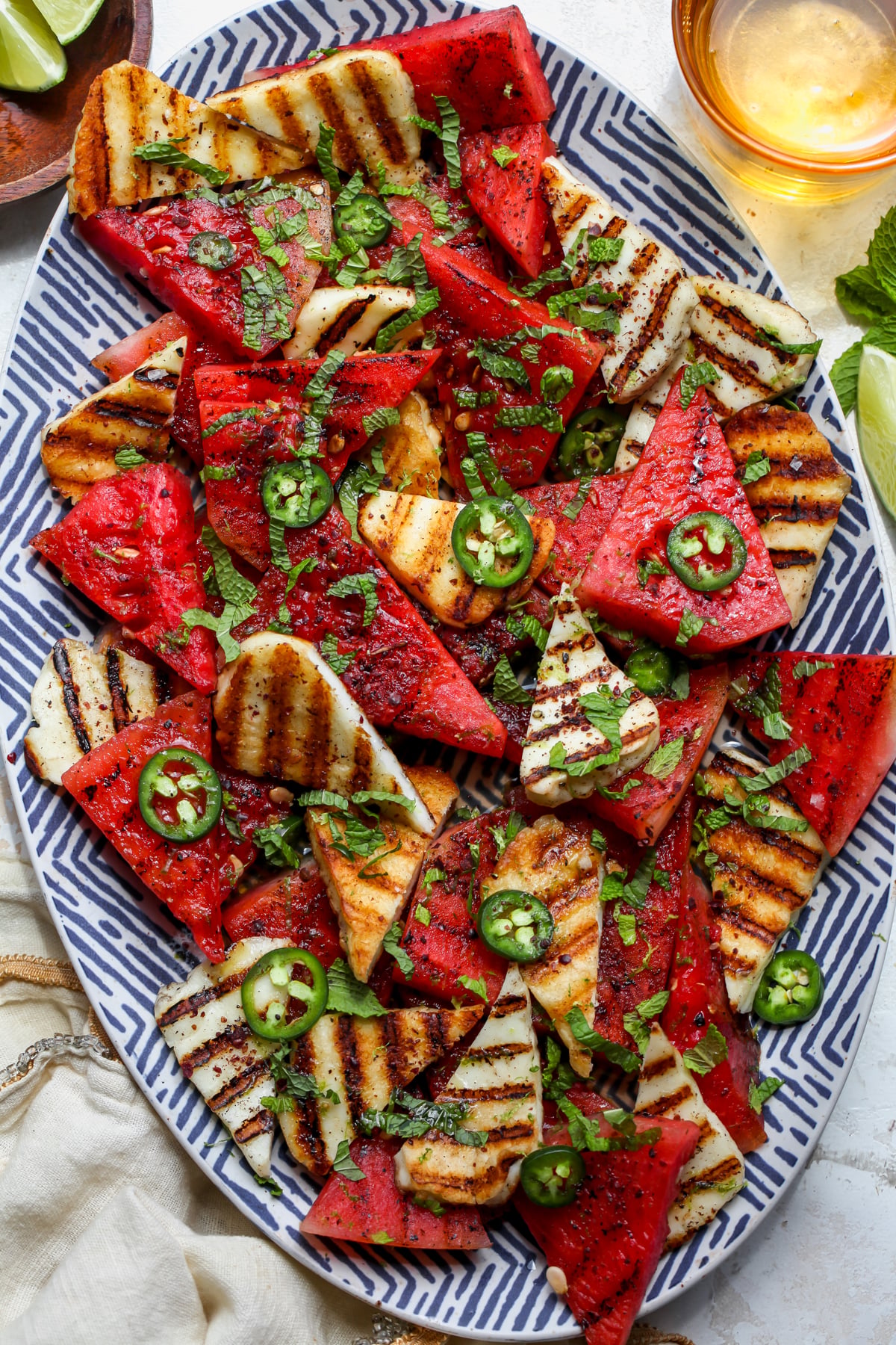 Grilled halloumi and watermelon salad arranged on a blue and white platter topped with jalapeño, mint, and sumac.