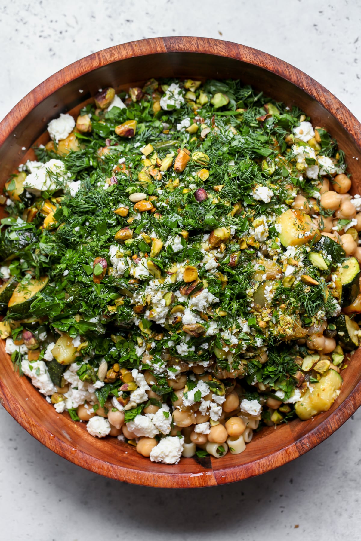 All of the salad ingredients being added to a large wooden serving bowl.