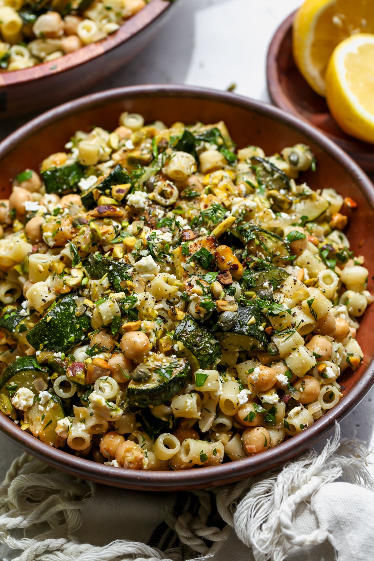 Zucchini feta salad topped with pistachios and herbs styled in a maroon bowl.