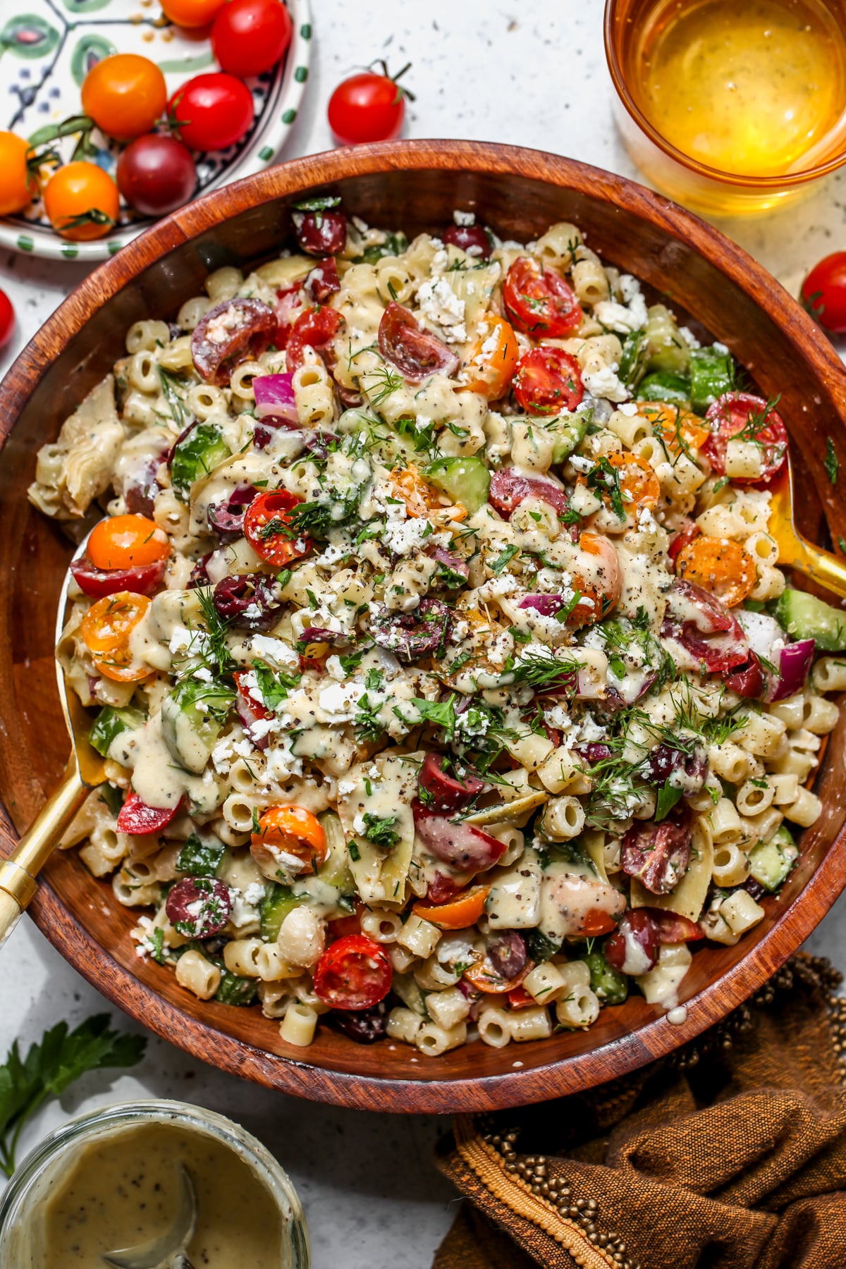Chopped Greek Pasta Salad styled in a large wooden bowl topped with fresh dill and feta cheese crumbles.