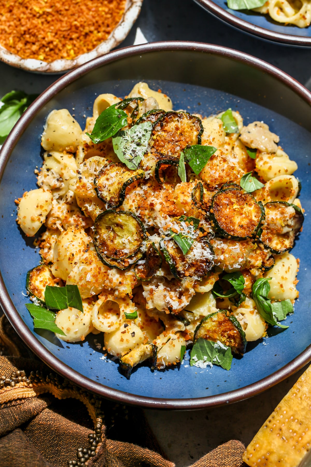 Caramelized Zucchini and Sausage Pasta styled in a blue bowl topped with panko, basil, and Parmesan.