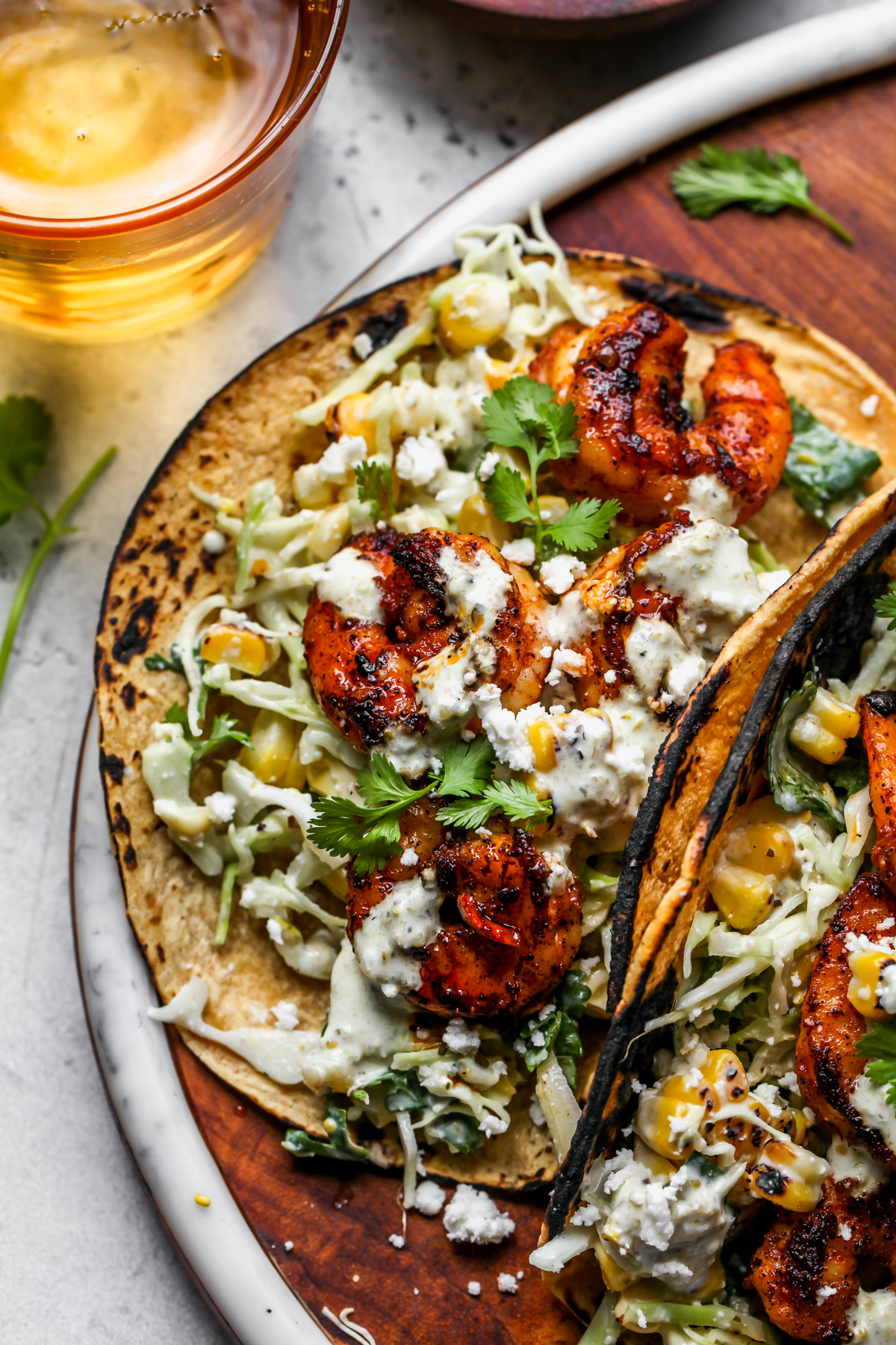 Fully assembled shrimp tacos arranged on a wooden platter with a gold glass of water next to them.