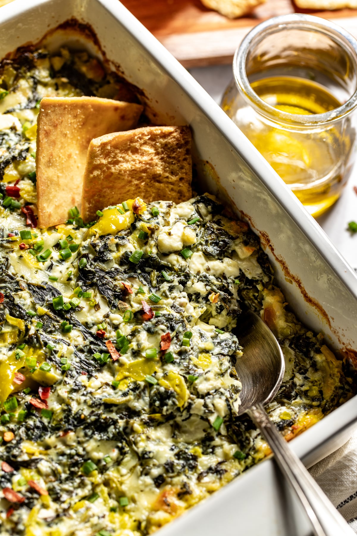 Pita chips scooping a portion of baked feta dip out of a baking dish.