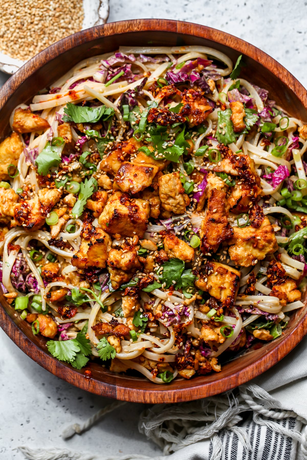 Sesame rice noodle salad styled in a wooden salad bowl on a gray surface.