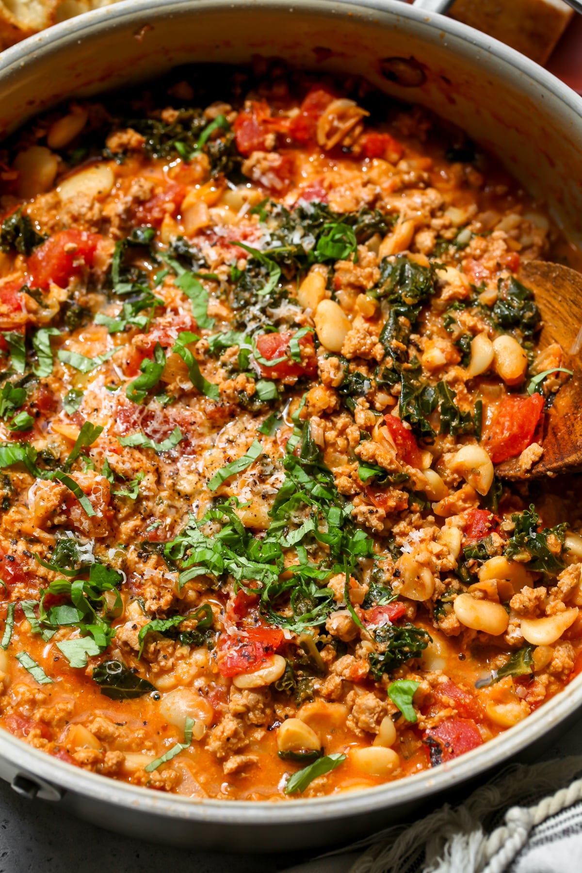 Tuscan Turkey and White Bean Skillet topped with fresh basil leaves and Parmesan styled in a white sauté pan.
