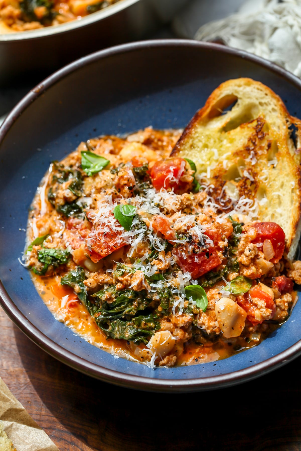 Tuscan white bean skillet served in a blue serving bowl with a chunk of grilled bread on the side.