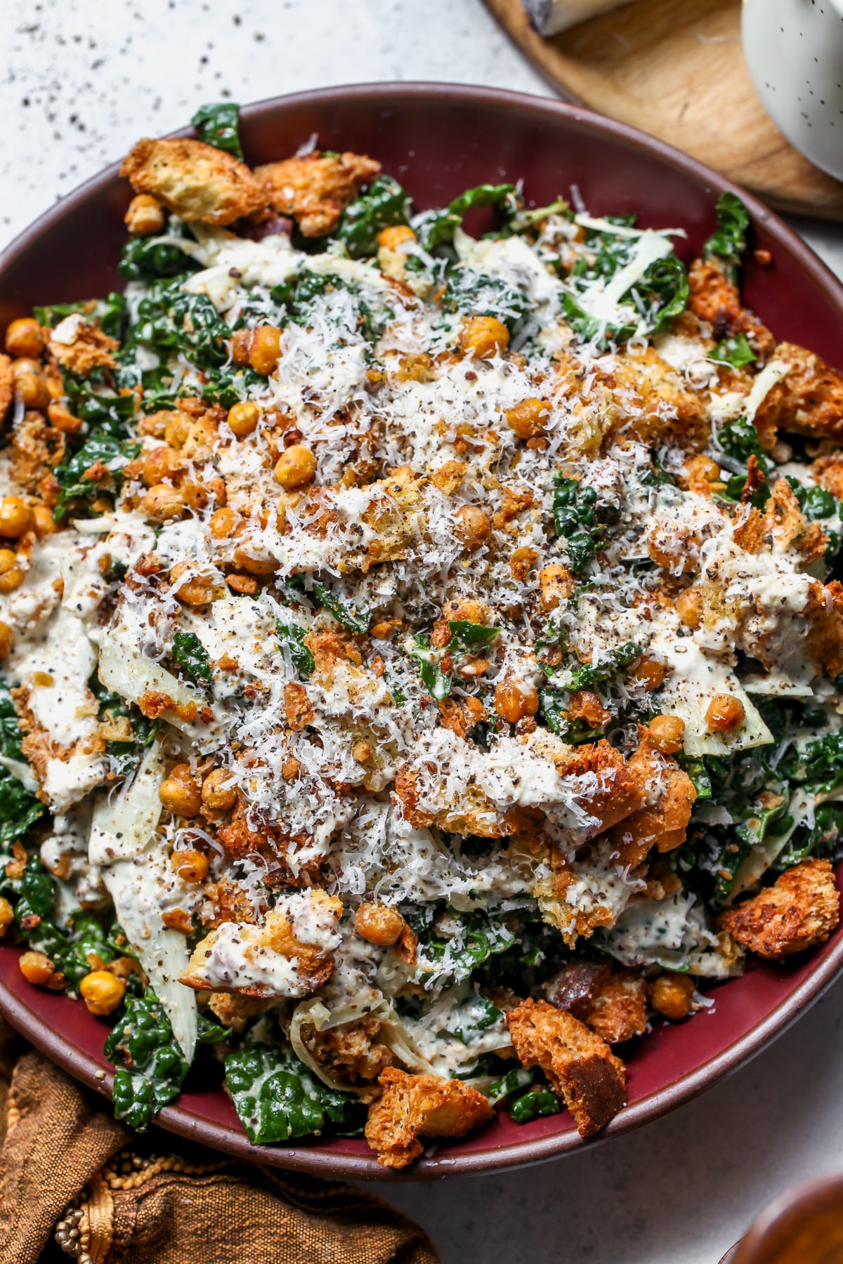 Cacio e Pepe Kale and Fennel Caesar Salad styled in a large maroon serving bowl on a gray surface.