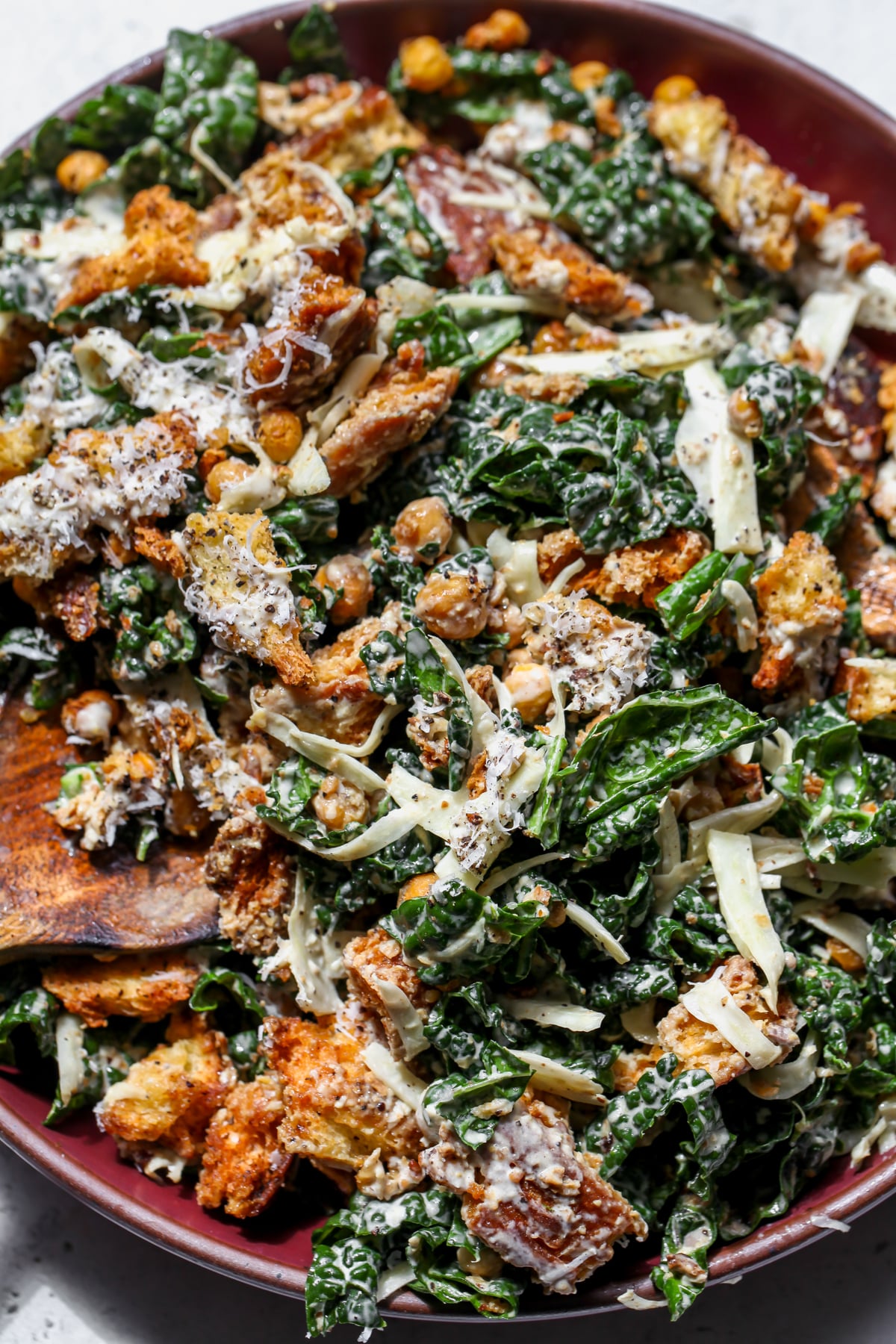 Kale and Fennel Caesar Salad being mixed in a large maroon bowl.