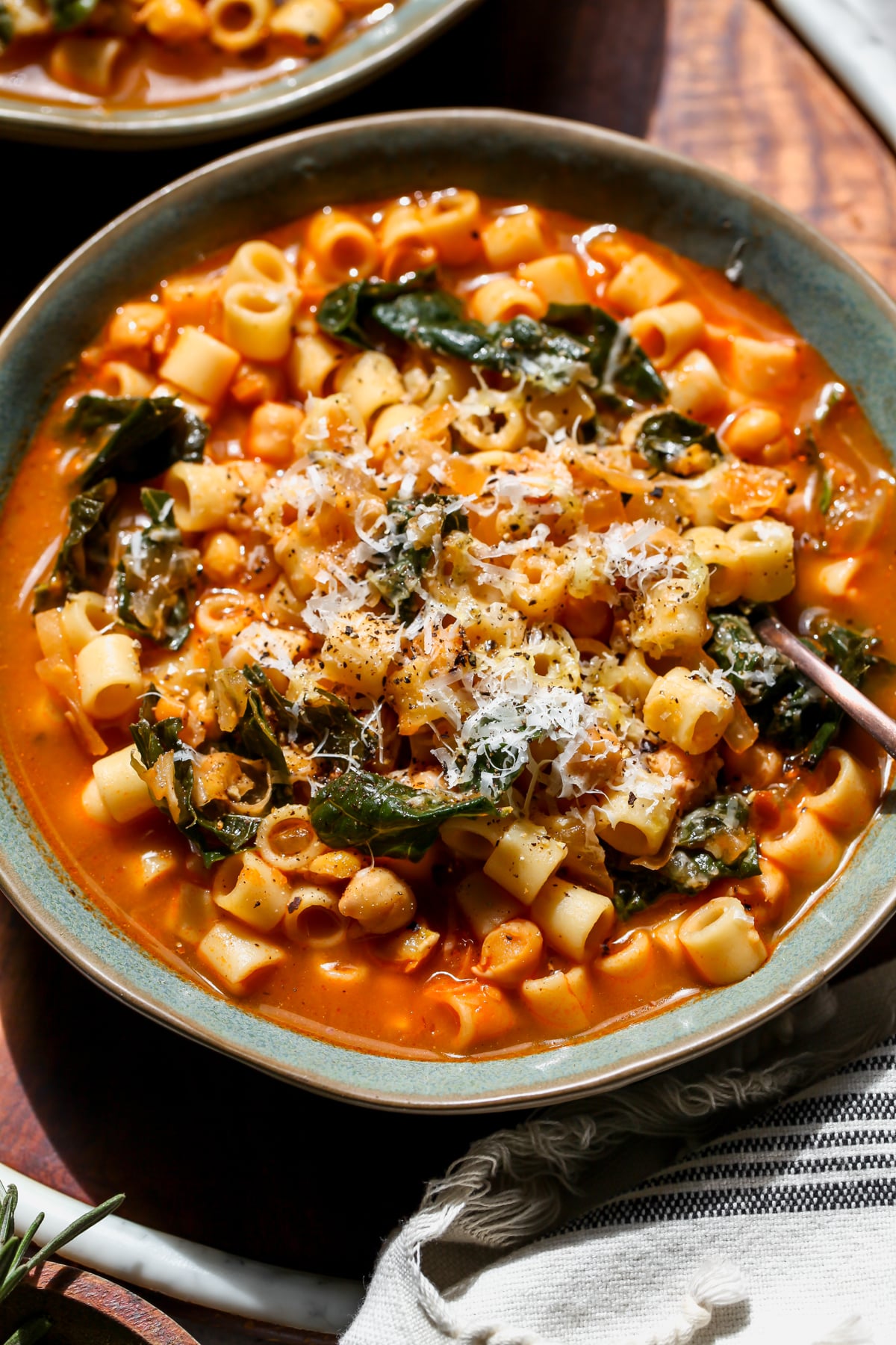 Pasta e Ceci styled in a blue bowl on a wooden tray with a spoon resting on the right side.