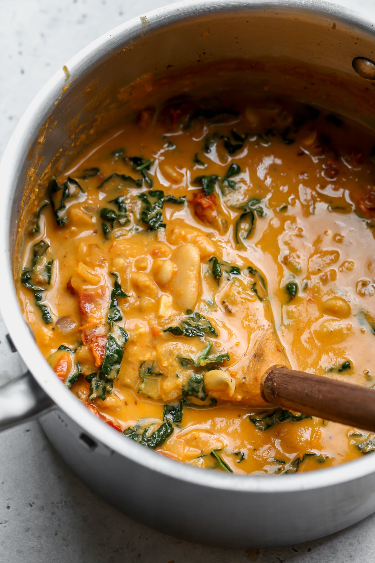 Tuscan butter bean soup being stirred in a pot with a wooden ladle.