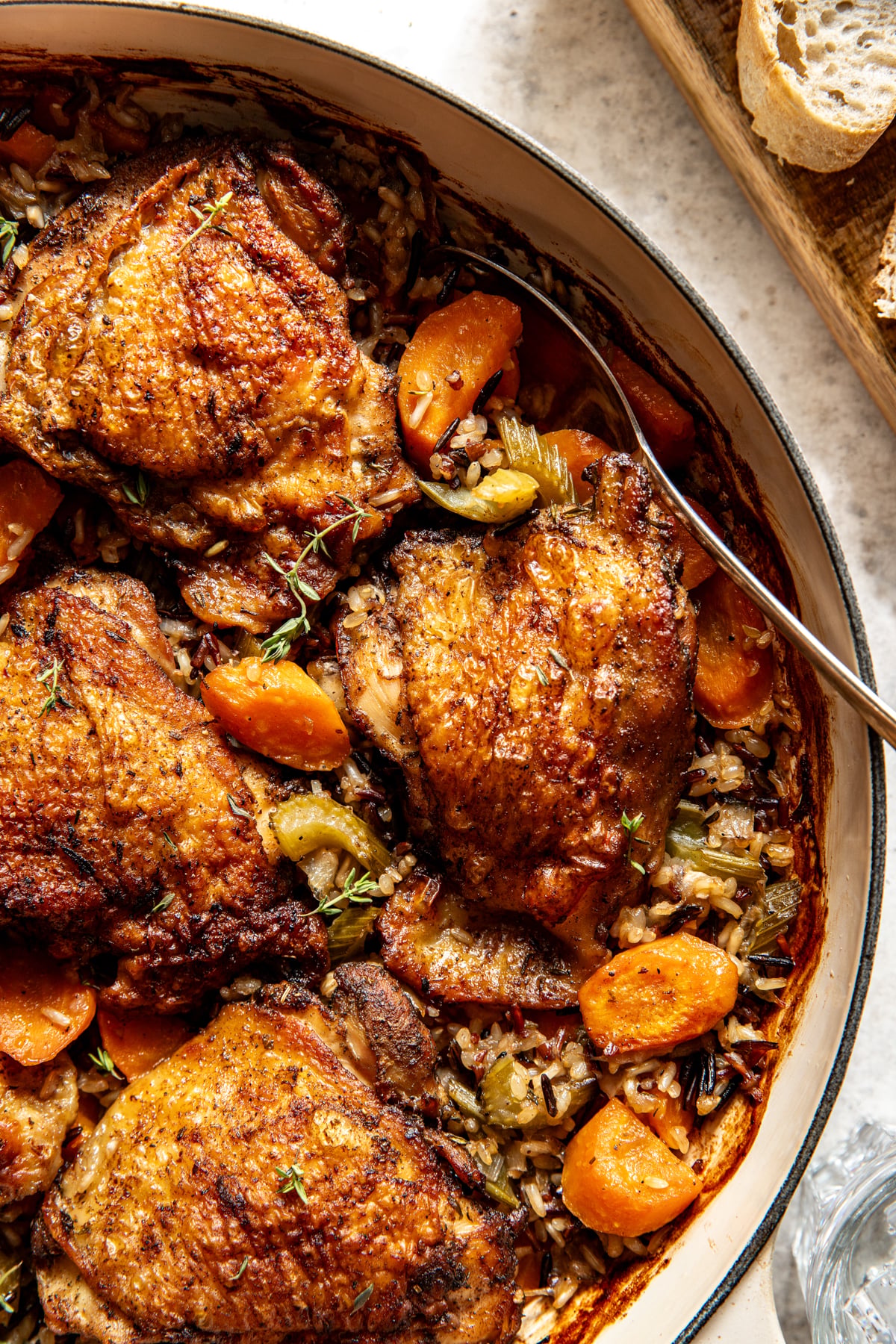A spoon digging into a pan of roasted chicken thighs, wild rice, and veggies.
