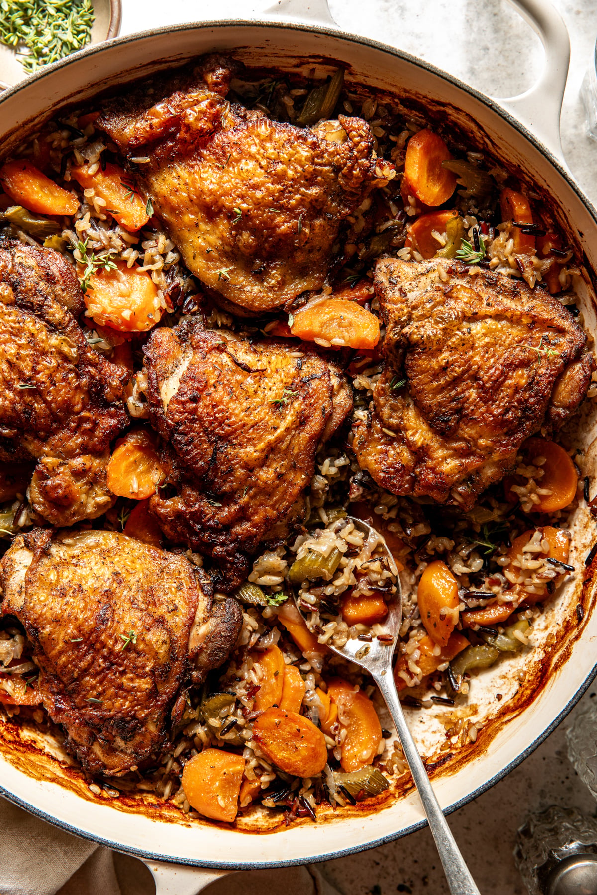 Herby chicken and wild rice styled in a tan pot with a spoon resting on the lower right side.