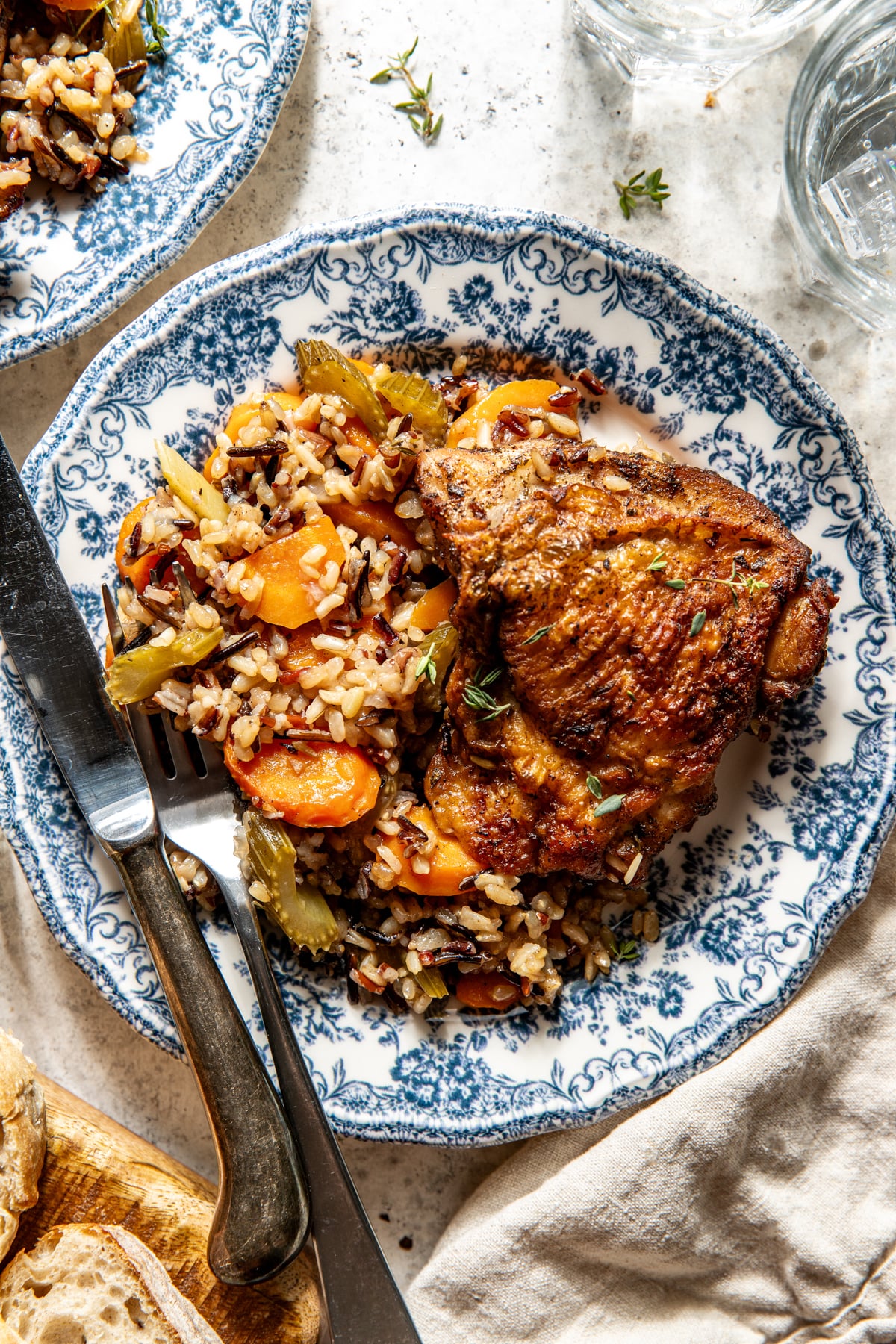 One chicken thigh with wild rice and veggies styled on a white and blue floral plate.