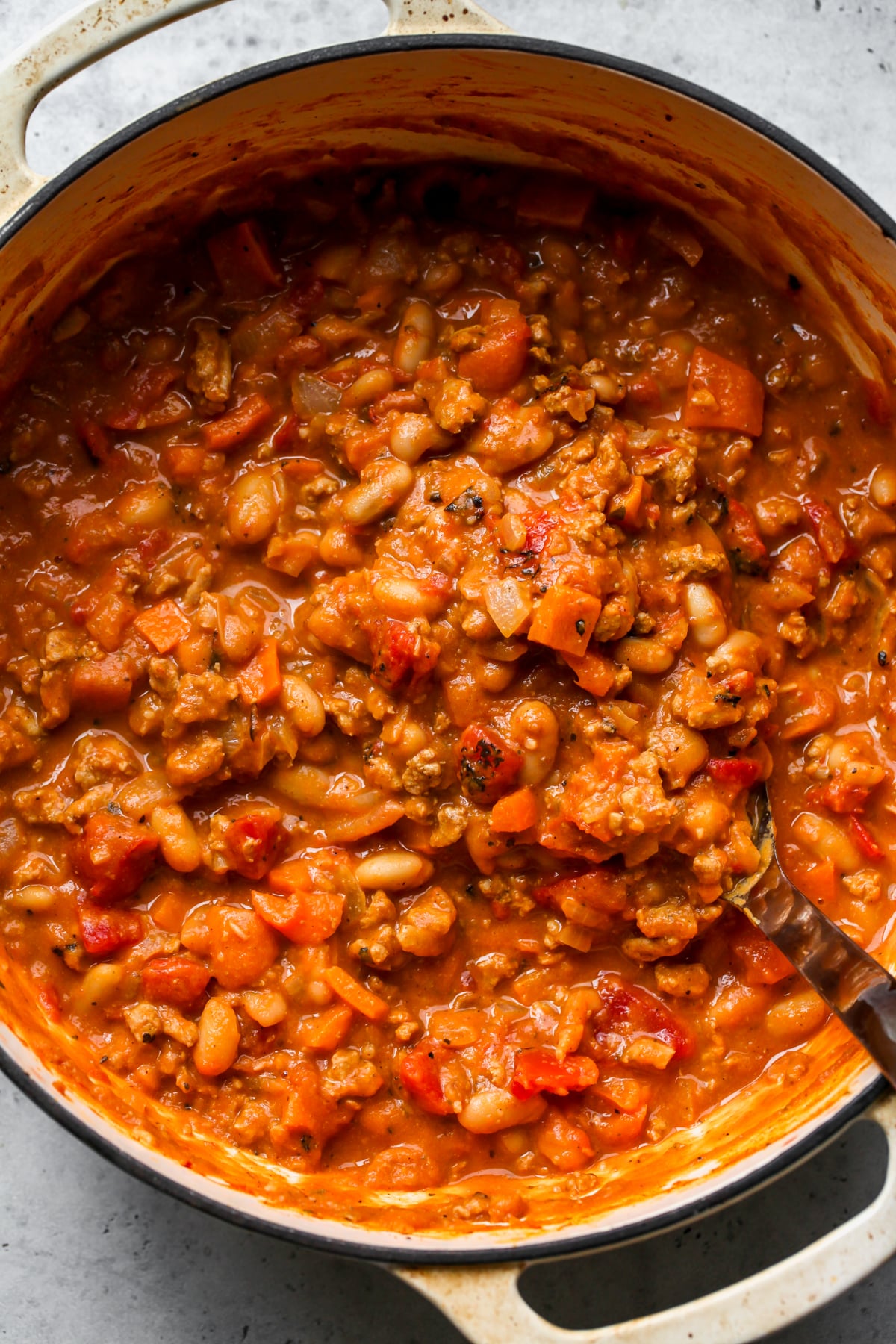 A tan Dutch oven filled with chili being stirred with a ladle.
