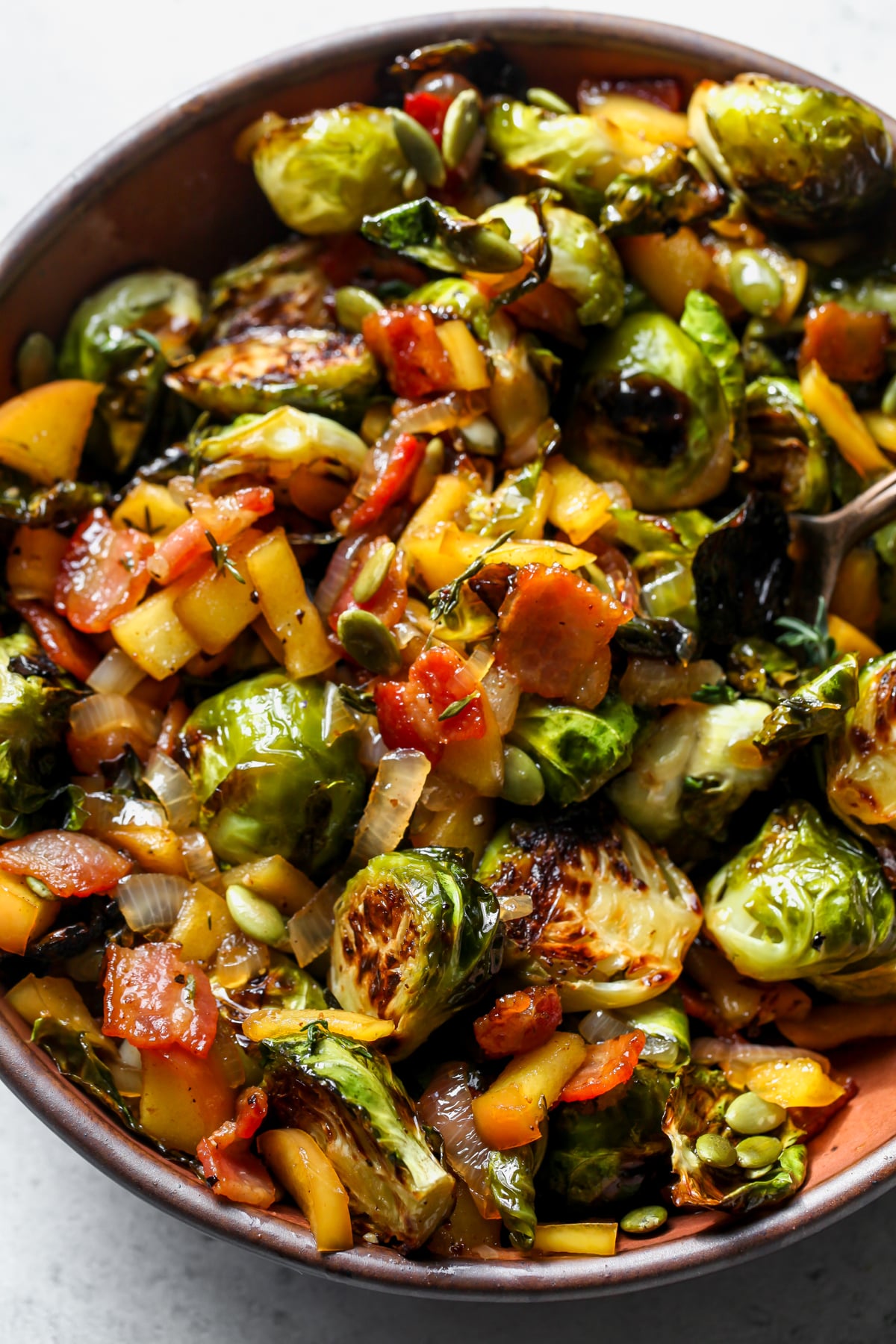 Cider glazed Brussels sprouts styled in a maroon serving bowl.