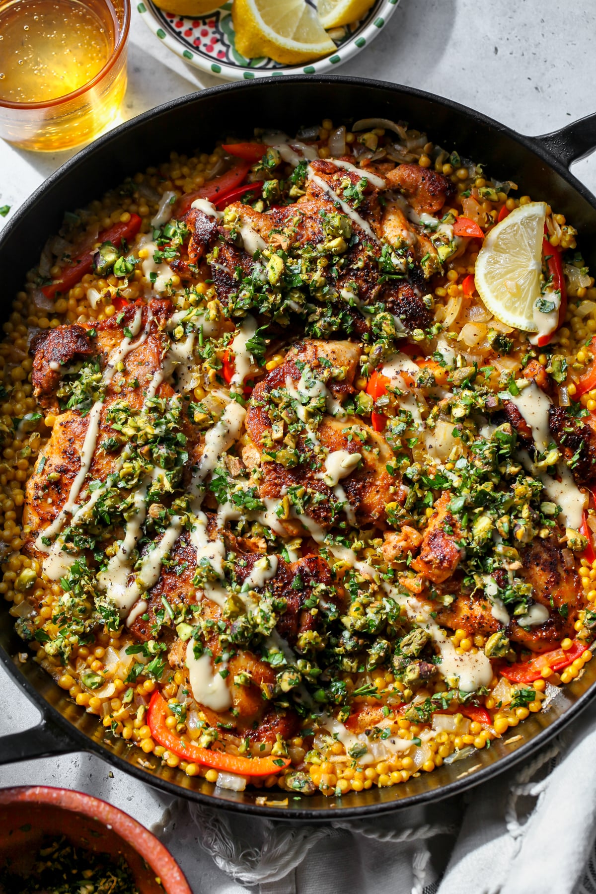 Mediterranean Chicken and Couscous topped with Pistachio Gremolata and Tahini-Honey in a large cast iron skillet.