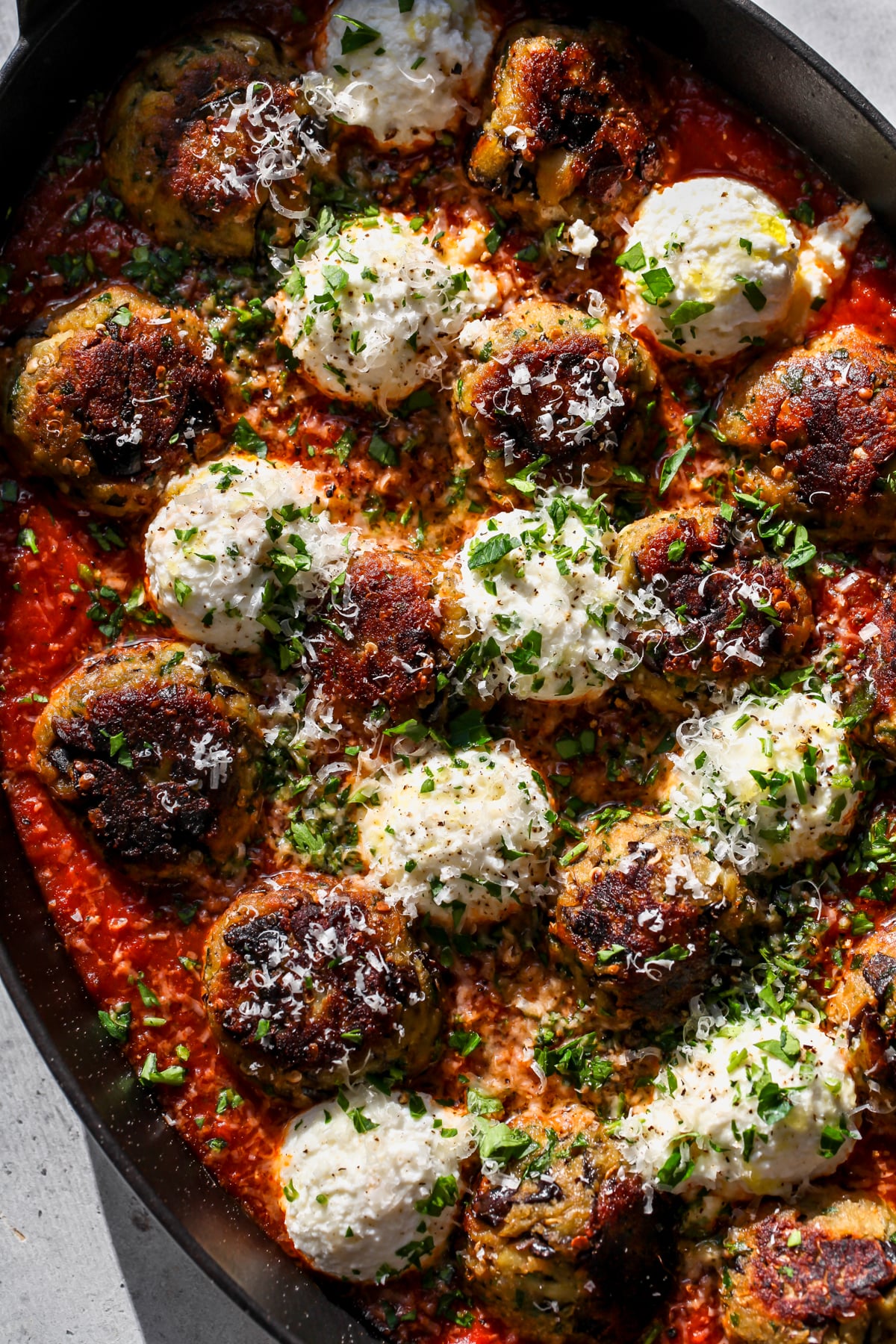 Eggplant Parmesan Meatballs styled in a pan with dollops of ricotta cheese, fresh parmesan, and parsley.