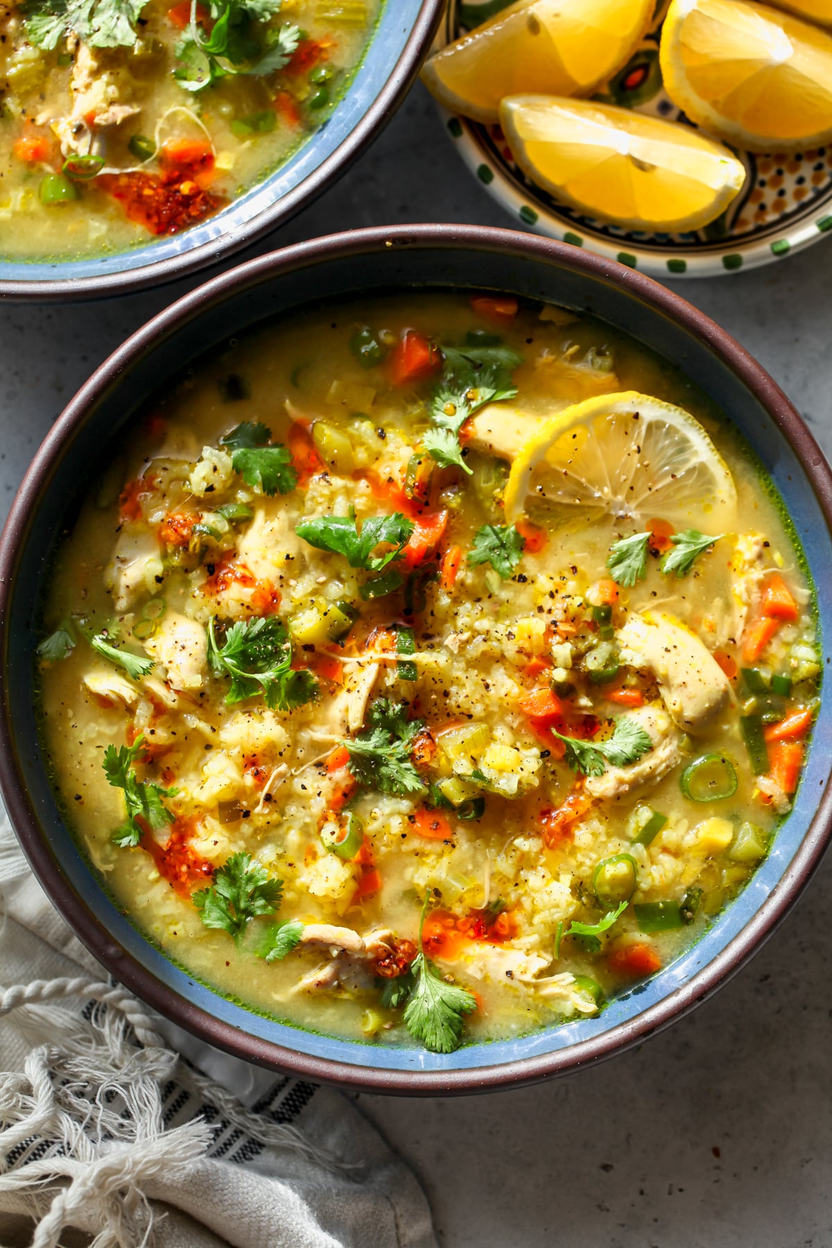 Immune-boosting chicken and rice soup styled in a blue bowl topped with lemon, cilantro, and chili oil.