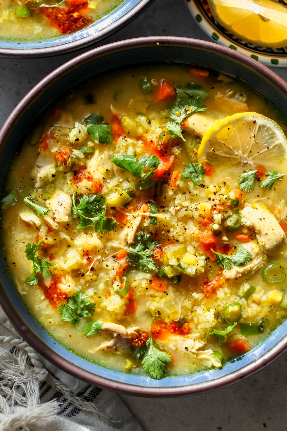 Immune-Boosting Chicken and Rice Soup styled in a blue bowl topped with a lemon slice, fresh cilantro, and chili crisp.