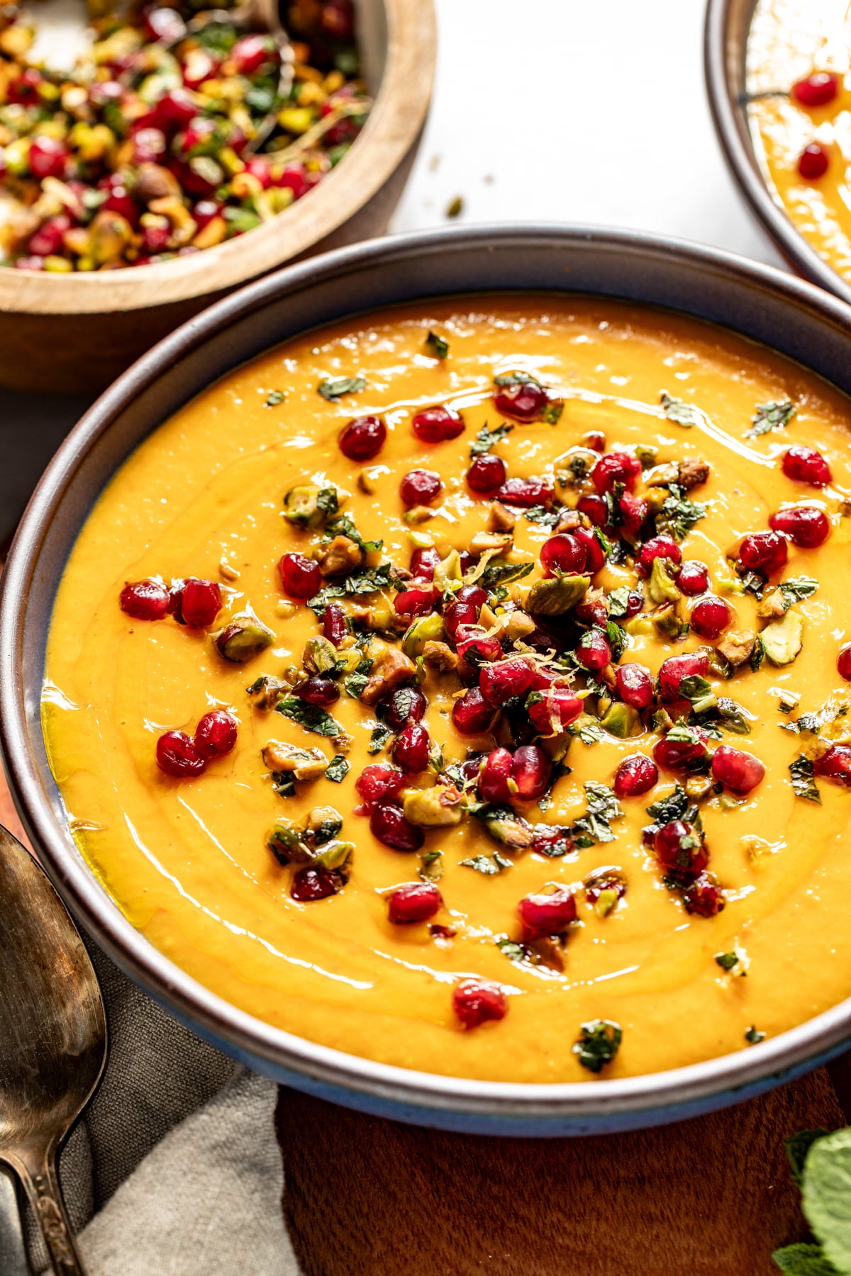 Butternut coconut milk soup topped with pomegranate and pistachio gremolata styled in a blue bowl.