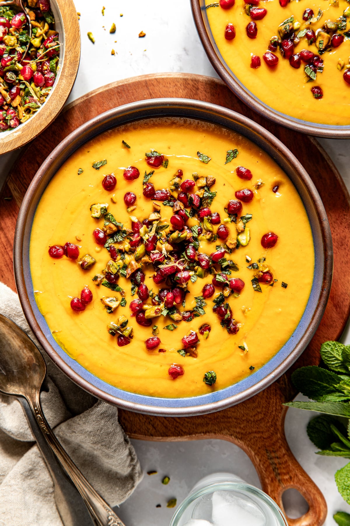 Golden butternut squash and coconut milk soup topped with pomegranate gremolata styled in a blue soup bowl.