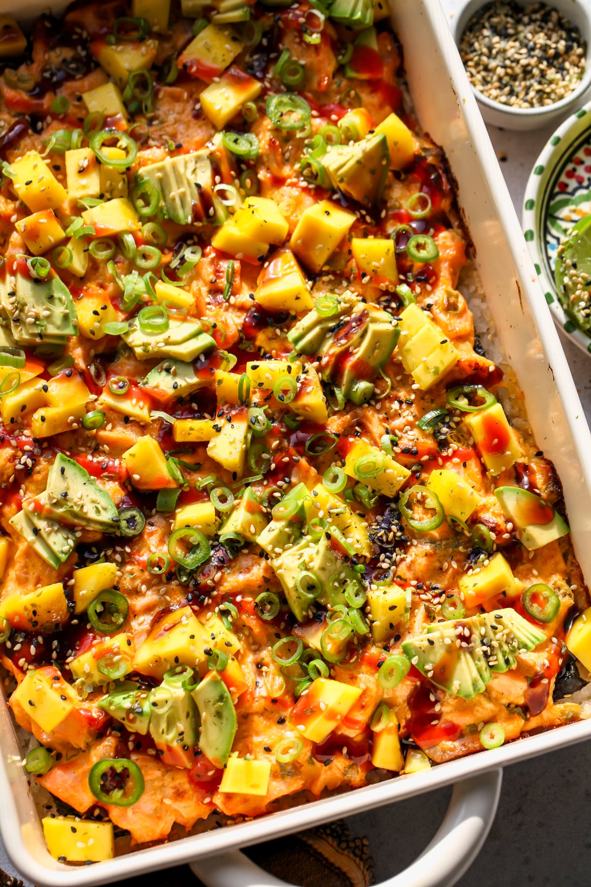 Spicy mango and salmon sushi bake styled in a casserole dish on a gray surface.