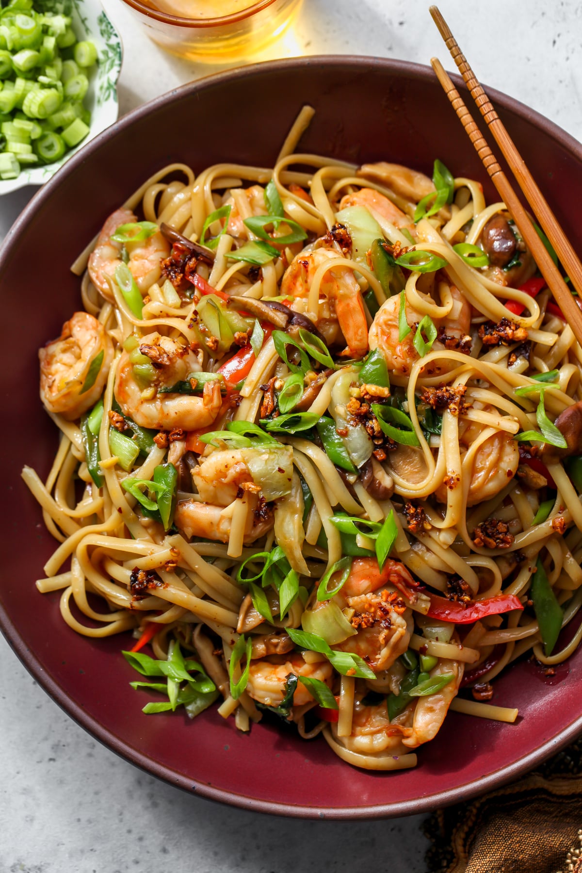 Shrimp and veggie Lo Mein styled in a maroon serving bowl with chopsticks resting on the upper right side.