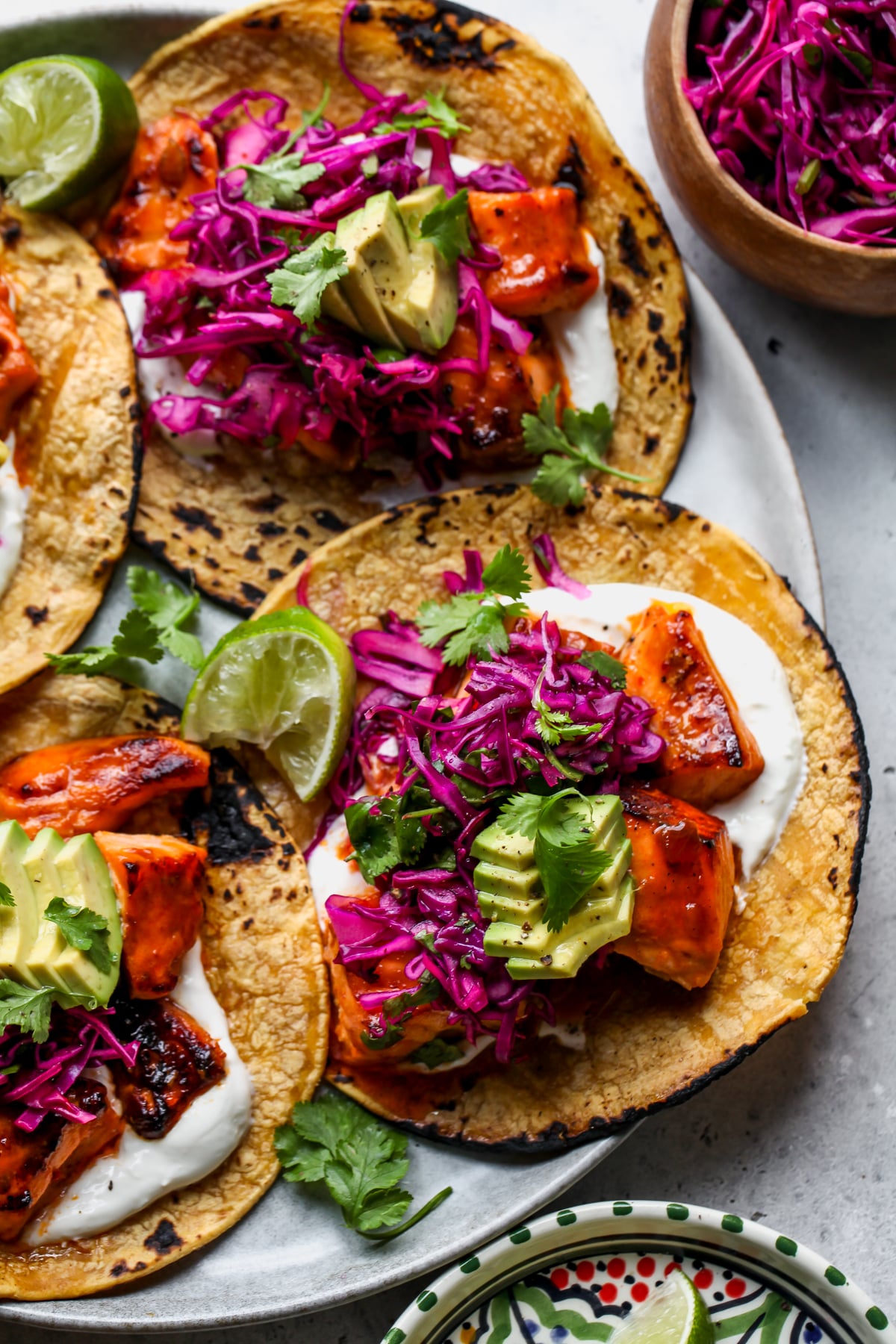 Chipotle salmon tacos topped with avocado slices and red cabbage slaw.