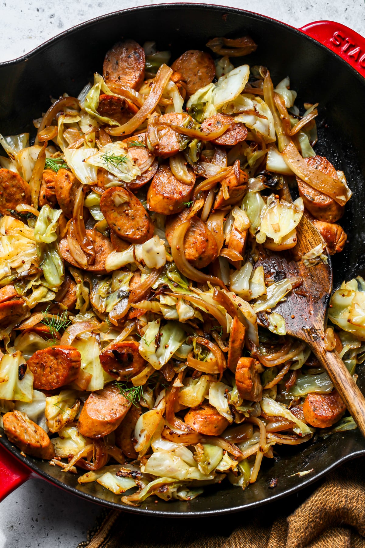 Chicken Sausage and Cabbage styled in a cast iron skillet with a wooden spoon resting on the right side.