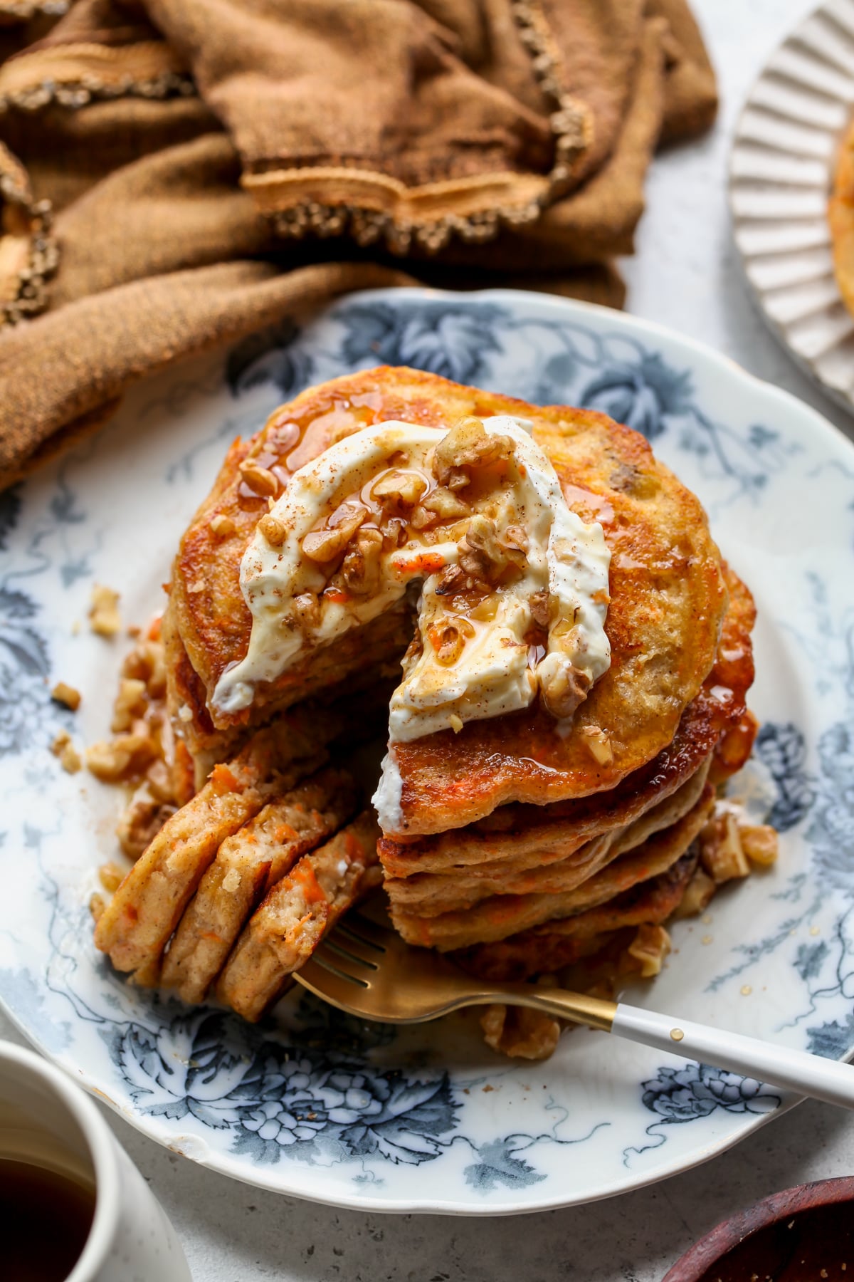 A stack of carrot cake protein pancakes on a white and blue floral plate with a fork resting on the right side.